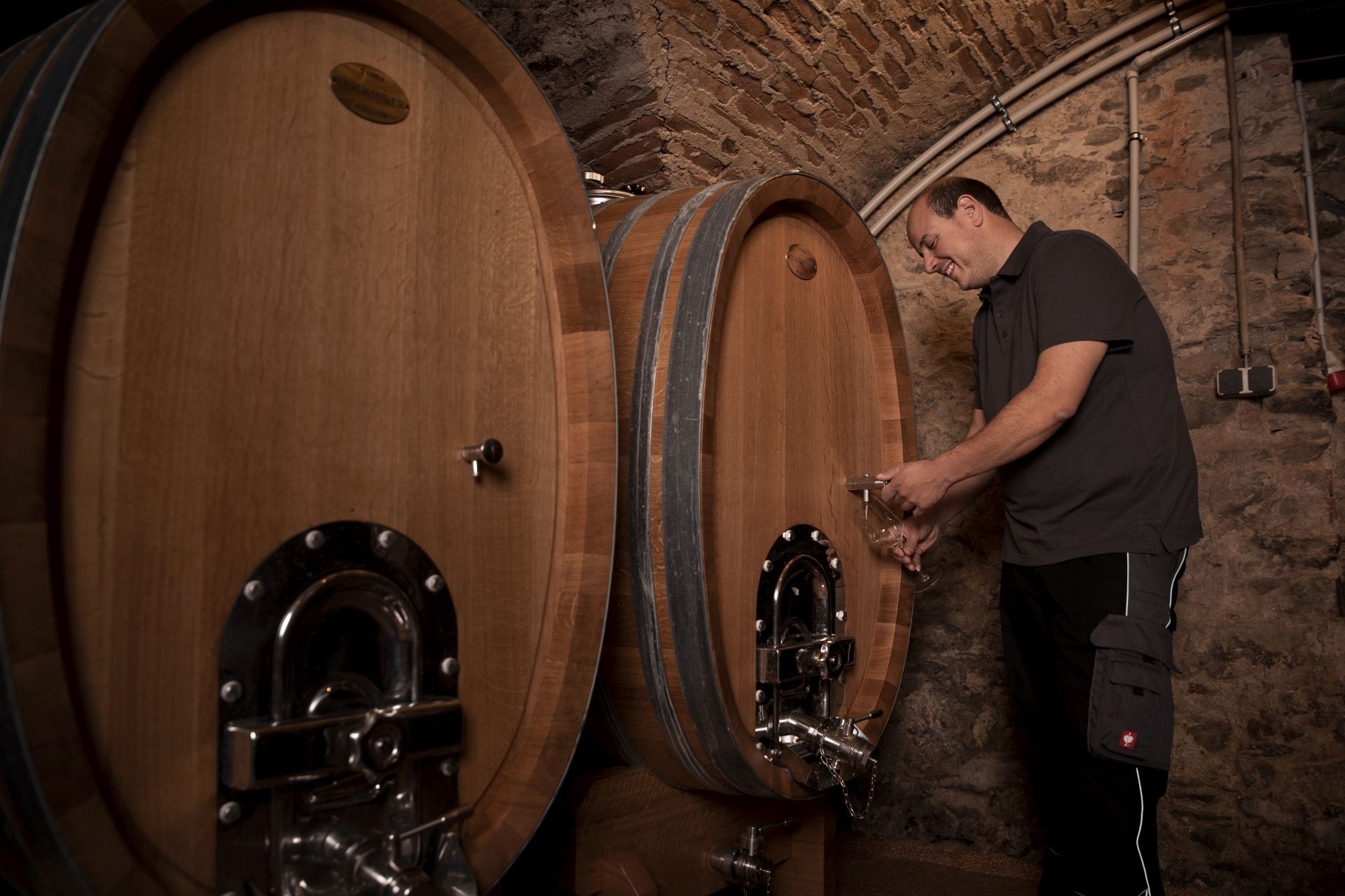 Ein Mann zapft Wein aus einem großen Holzfass in einem Weinkeller.