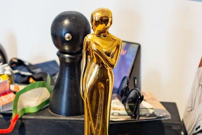 Regal mit Glasböden, darauf Bücher, eine goldene Statue, ein Stempel, Zerr-Gurt, Sonnenbrille und Magazinen.