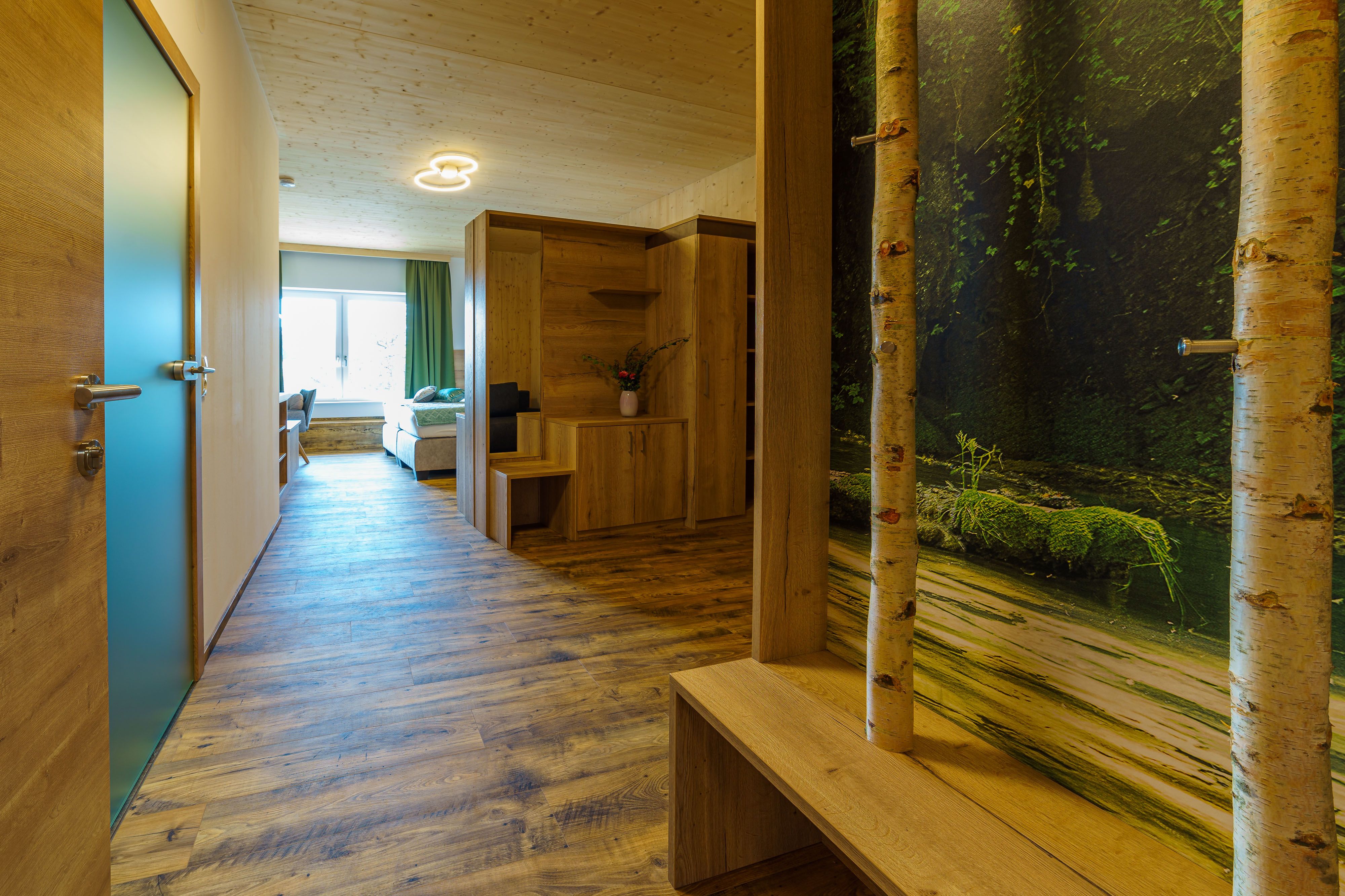 Innenansicht eines modernen Apartments mit Holzboden, Holzmöbeln und einem großen Fenster.