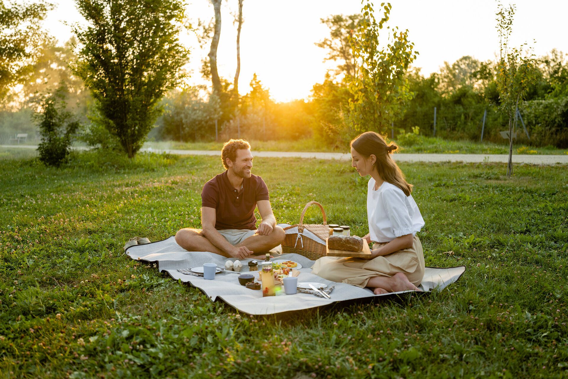 Ein romantisches Picknick im Grünen, umgeben von der sanften Abendsonne, lädt dazu ein, die Seele baumeln zu lassen. Die Wiese ist mit einer bunten Decke geschmückt, auf der köstliche Leckereien und erfrischende Getränke bereitstehen. Hier in der Natur, zwischen Bäumen und blühenden Pflanzen, wird der Sommer zu einem unvergesslichen Erlebnis.