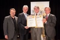 Vier Männer in Anzügen halten Zertifikate vor einem Banner.