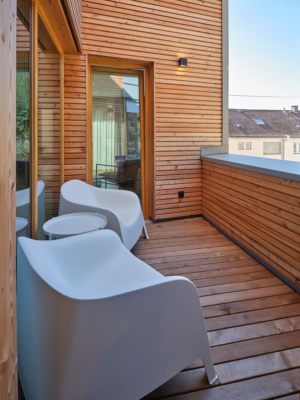 Moderner Balkon mit Holzwänden und weißen Stühlen.