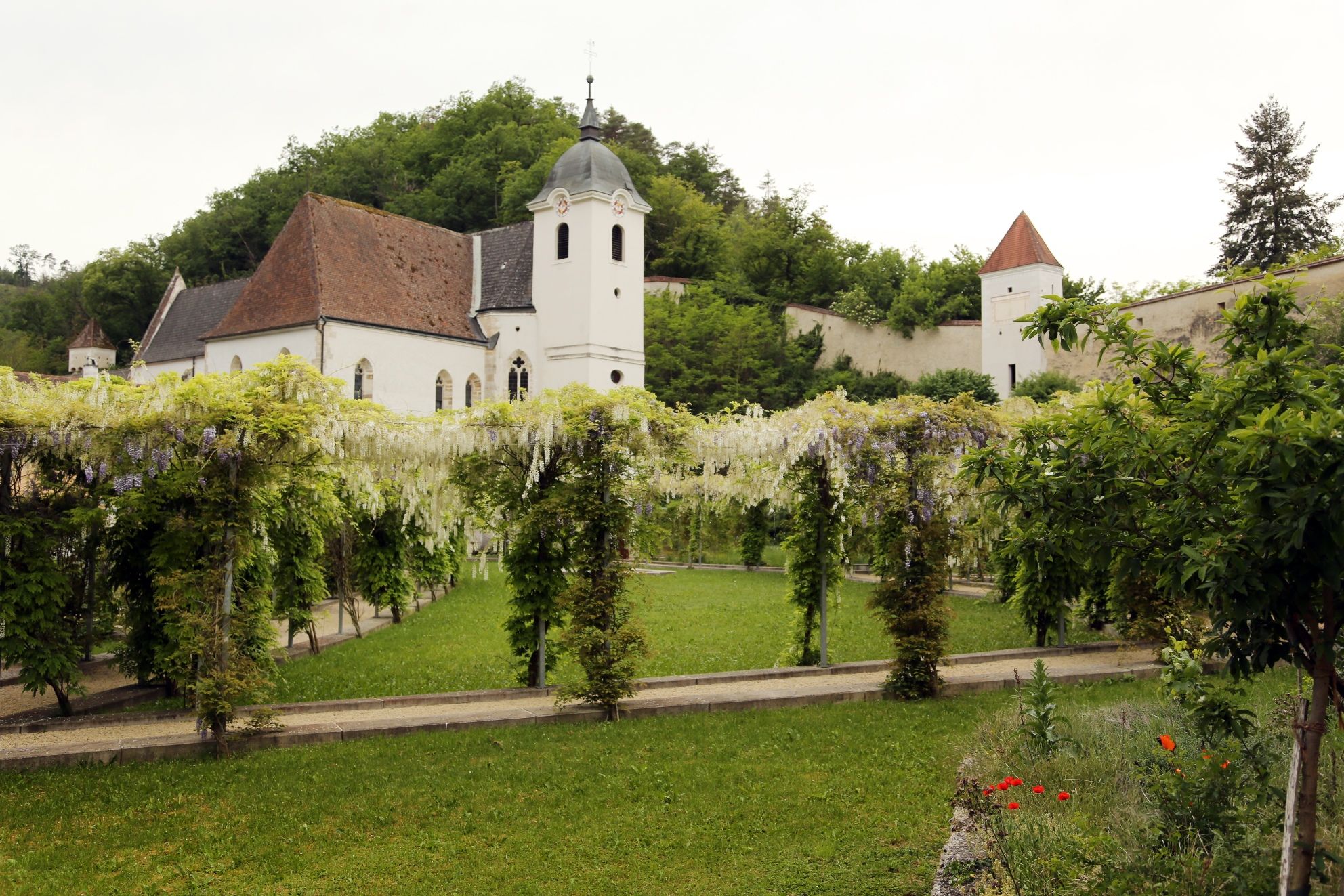Blick auf eine historische Kartause mit Garten und Pergola.