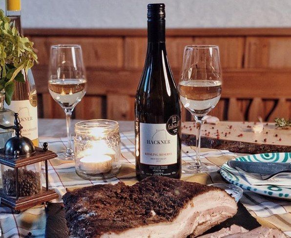 Tisch mit Weinflasche, zwei Gläsern, Kerze und Fleischgericht.