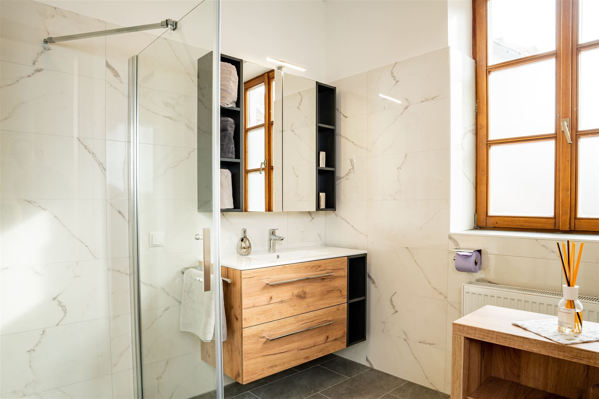 Modernes Badezimmer mit Holzmöbeln, großer Fensterfront und Glasdusche.