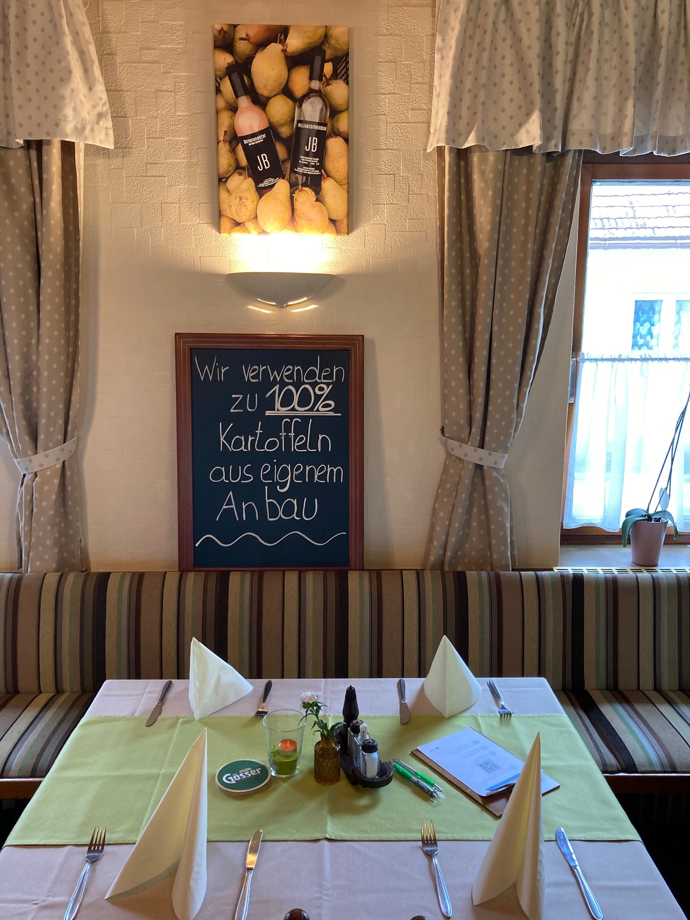 Gedeckter Tisch mit grüner Tischdecke, im Hintergrund ein Schild mit der Aufschrift: "Wir verwenden zu 100% Kartoffeln aus eigenem Anbau.