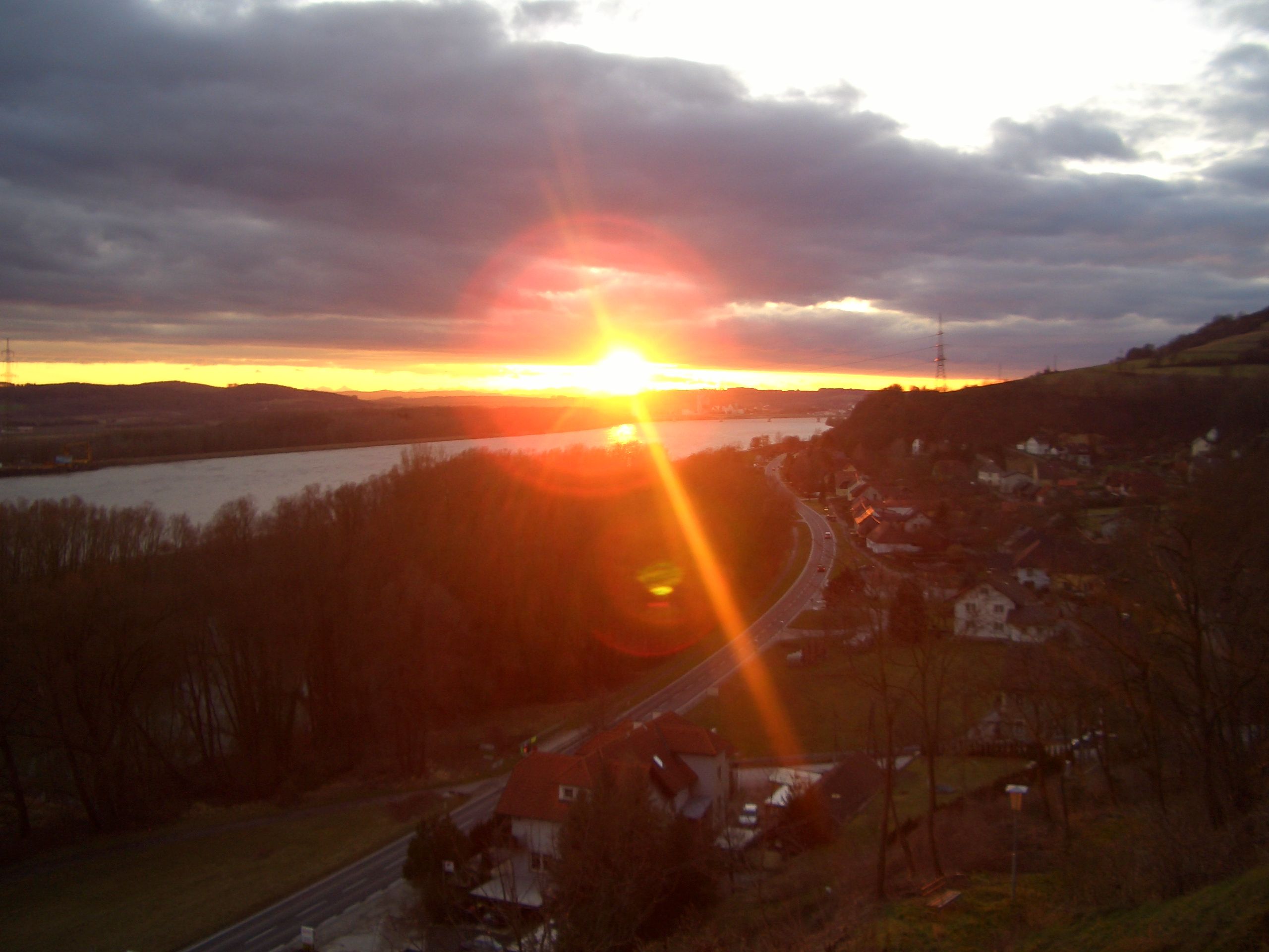 Sonnenuntergang über einer Landschaft mit Fluss und Straße.