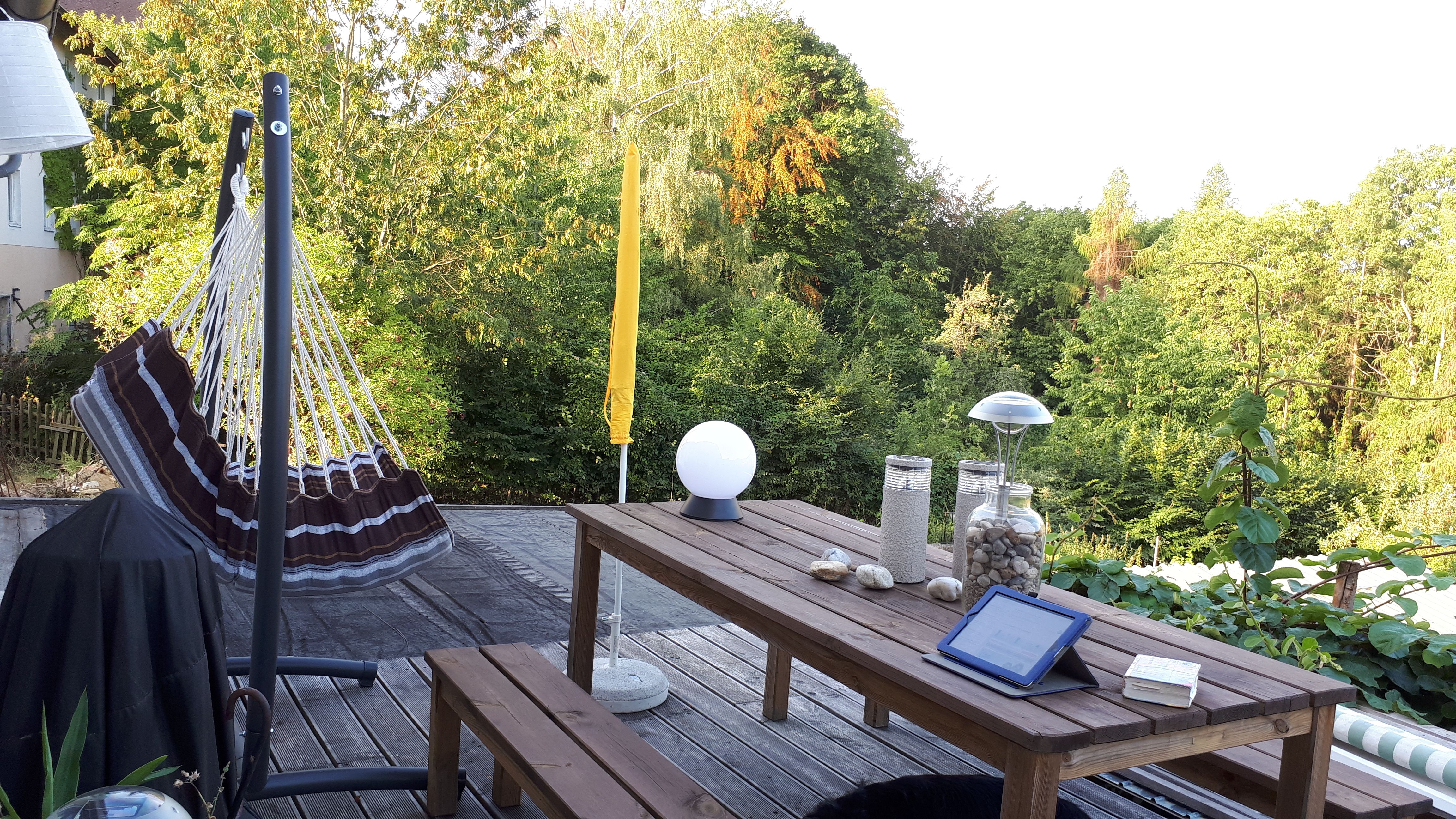 Terrasse mit Hängematte, Holztisch und Blick auf grüne Bäume.