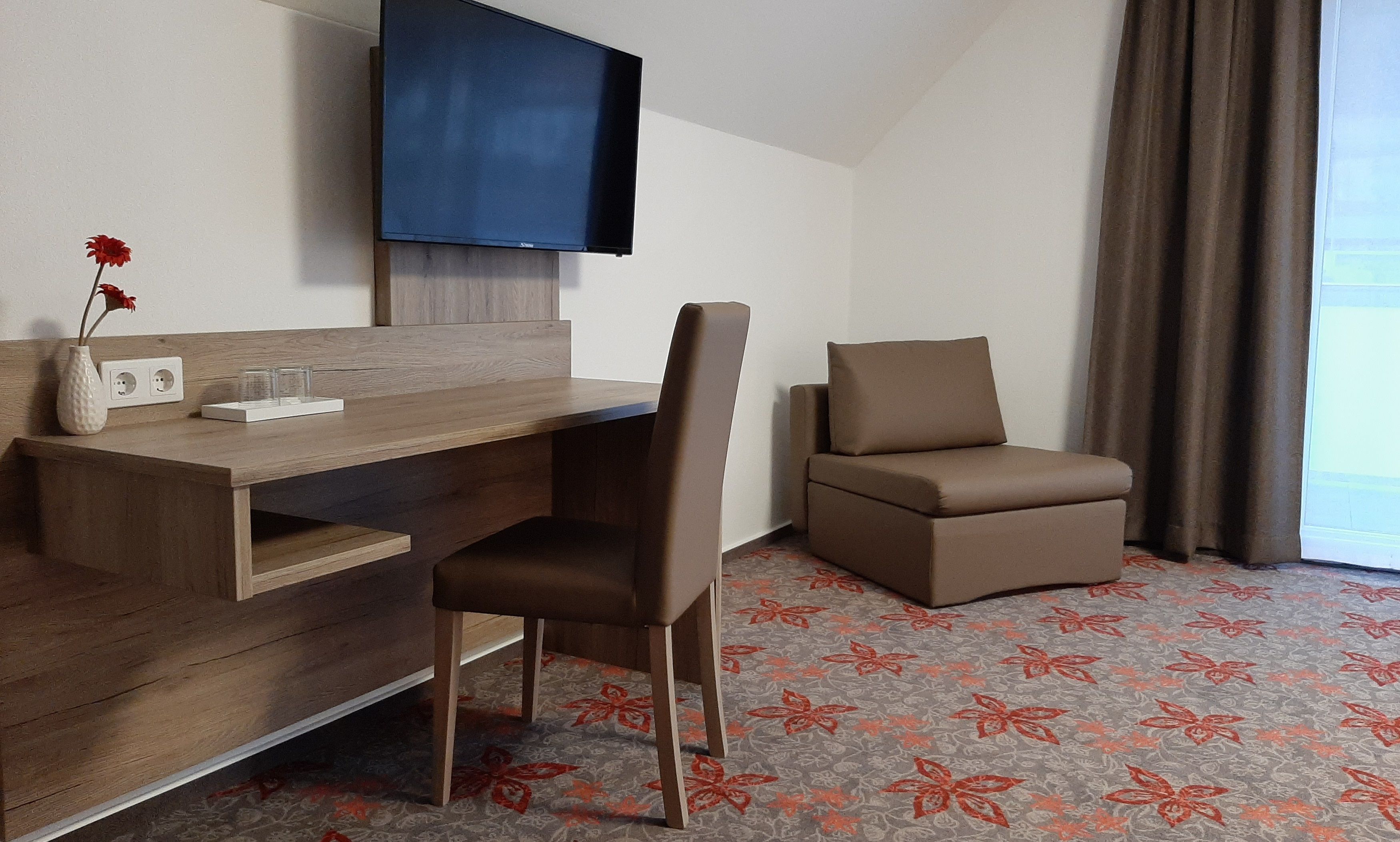 Hotelzimmer mit Schreibtisch, Stuhl, Fernseher und Sessel.