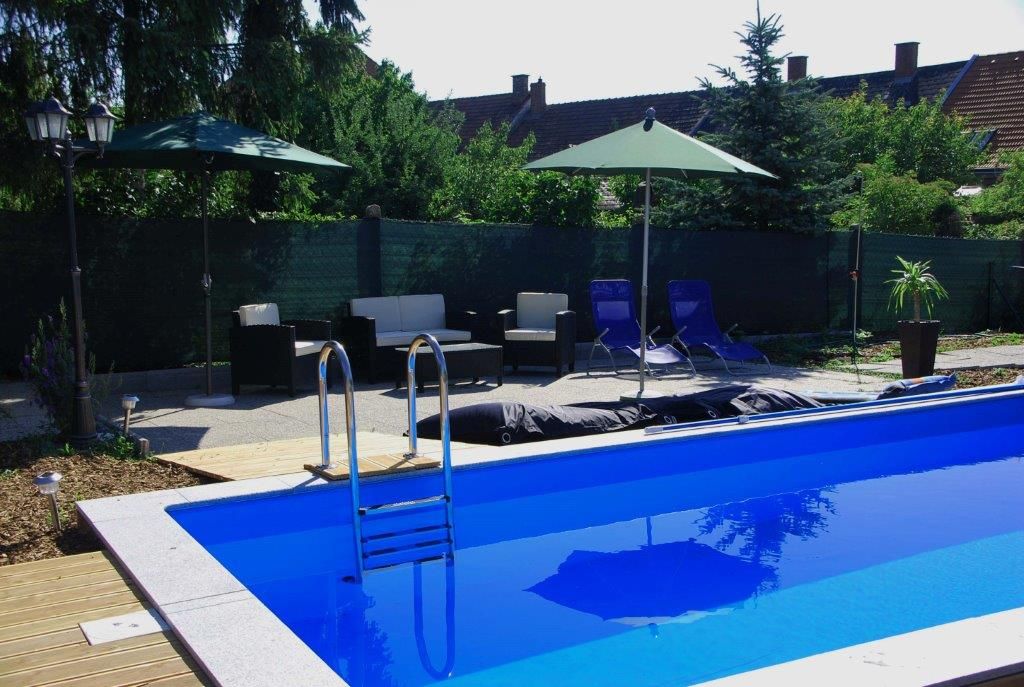 Ein Außenbereich mit einem blauen Pool, umgeben von Liegestühlen, Sonnenschirmen und Gartenmöbeln.