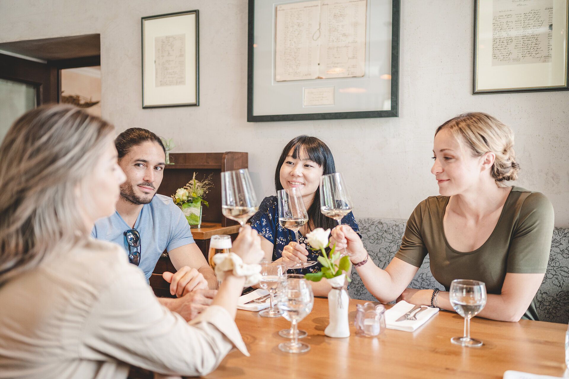 Vier Personen sitzen an einem Tisch und prosten sich mit Weißweingläsern zu.