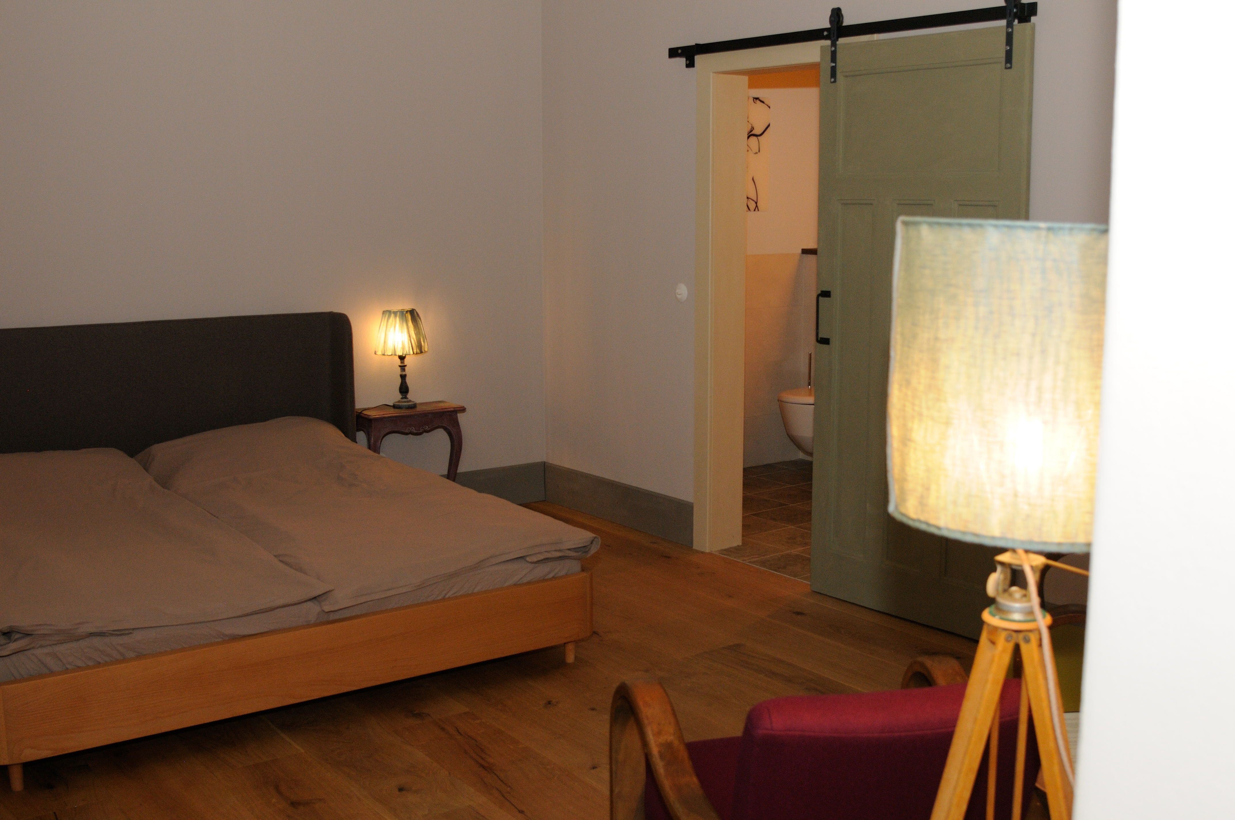 Ein gemütliches Schlafzimmer mit Doppelbett, Nachttischlampe und Schiebetür zum Badezimmer.
