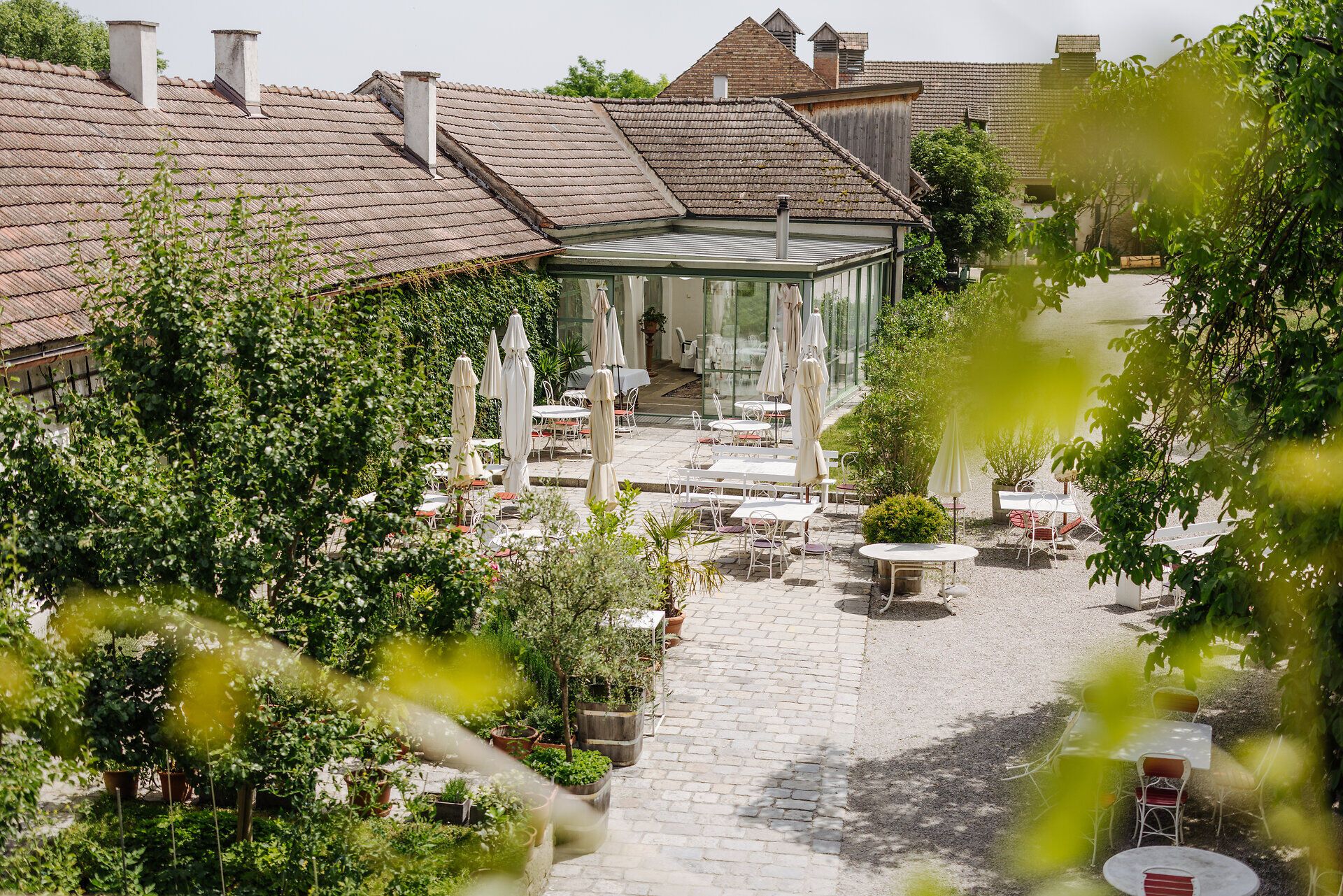 Umgeben von üppigem Grün und blühenden Pflanzen lädt die einladende Terrasse des Restaurants zum Verweilen ein. Hier genießen Gäste die frische Luft und die malerische Aussicht auf die sanften Hügel der Umgebung, während sie kulinarische Köstlichkeiten probieren.