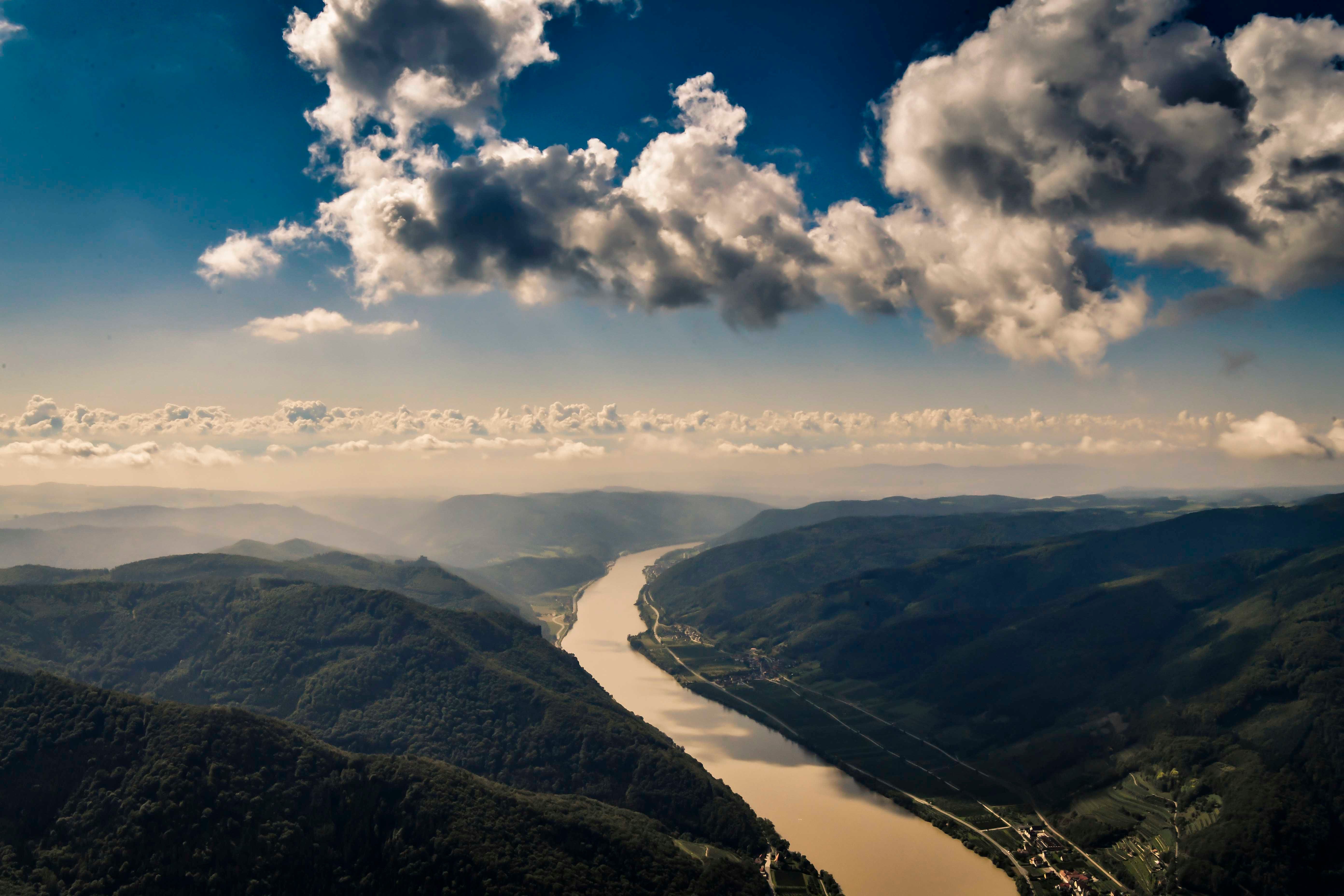 Landschaft mit Fluss und Bergen unter bewölktem Himmel.