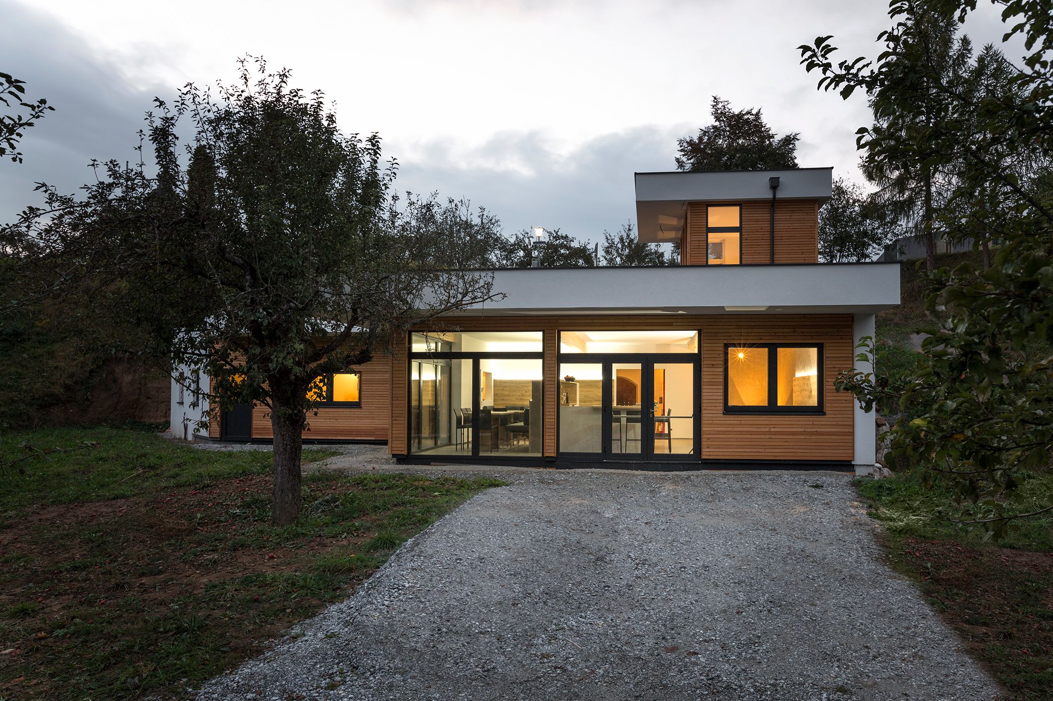 Außenansicht einer modernen Käserei mit großen Fenstern und Holzverkleidung, umgeben von Bäumen.