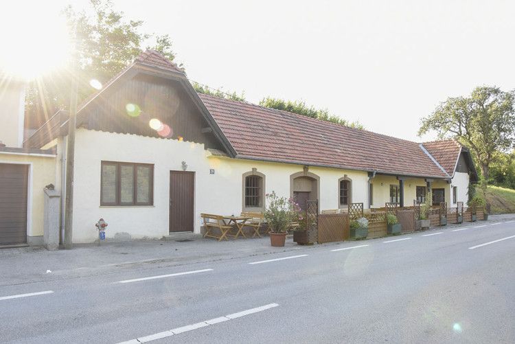 Ein traditionelles Gebäude mit roten Ziegeldächern und Holztischen vor der Tür, beleuchtet von der Sonne.