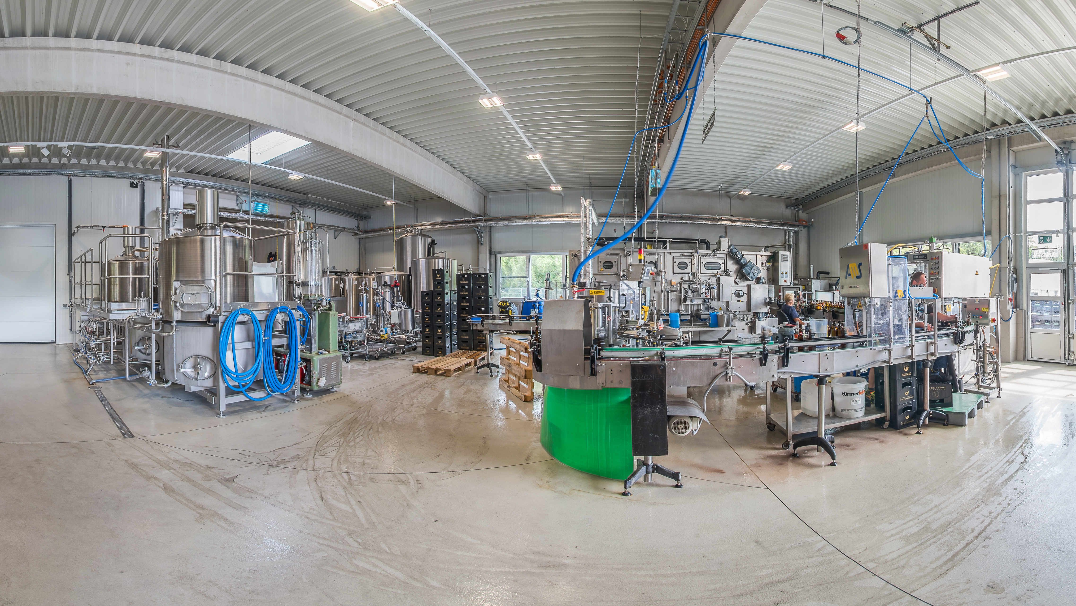 Interior view of a modern brewery with stainless steel tanks and bottling plants.