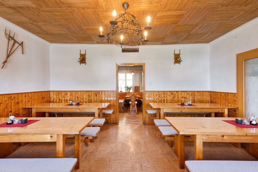 Innenansicht einer traditionellen Heurigenstube mit Holztischen und Bänken, Holzwandverkleidung und einem Kronleuchter an der Decke.