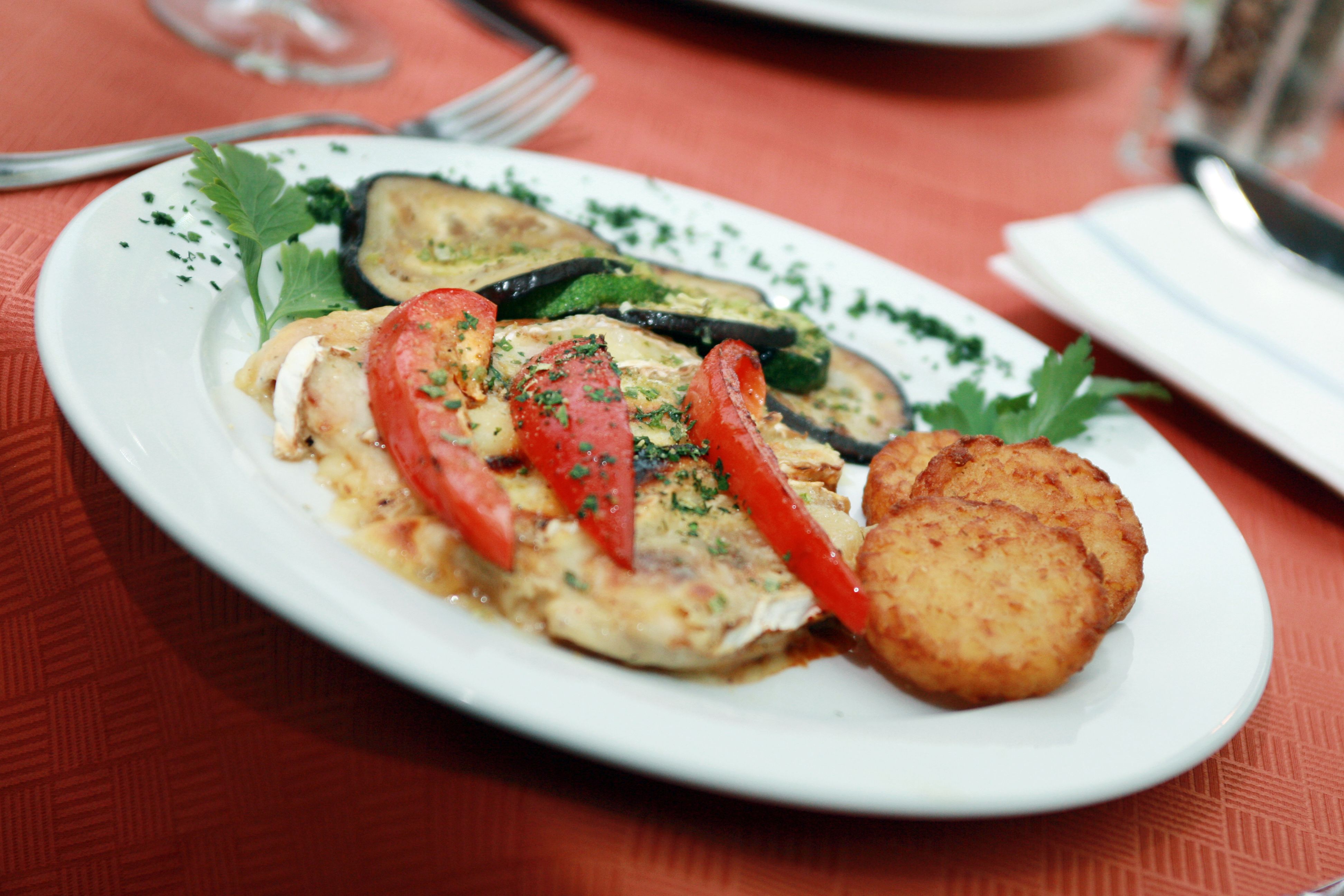 Ein Teller mit gebratenem Gemüse, Tomaten und Rösti auf einem roten Tisch.