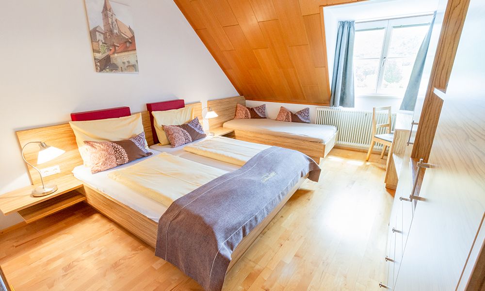 Gemütliches Gästezimmer mit Doppelbett, Einzelbett, Holzverkleidung und großem Fenster.