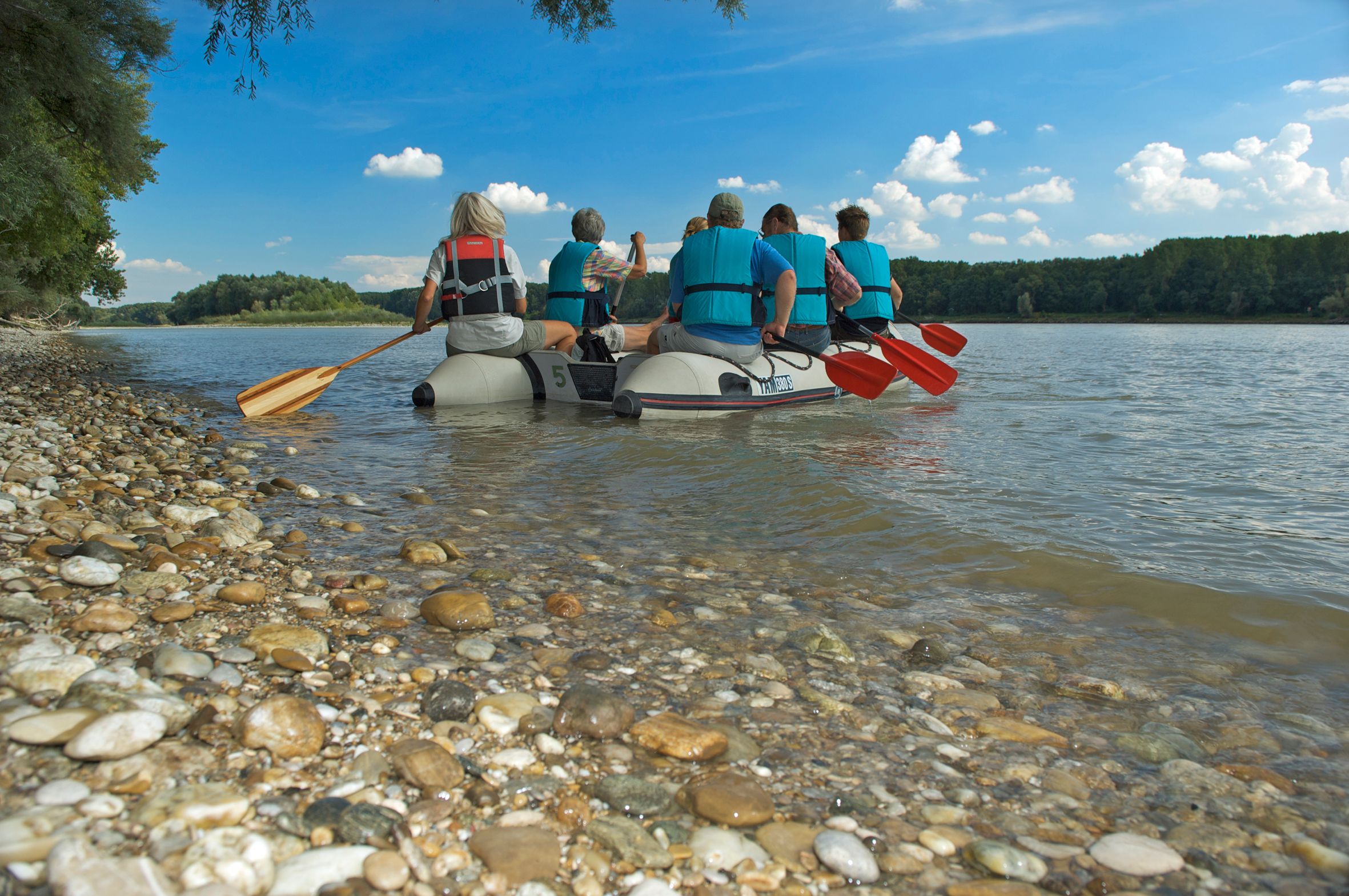 Schlauchboot mit Menschen die vom Ufer auf die Donau rudern. 