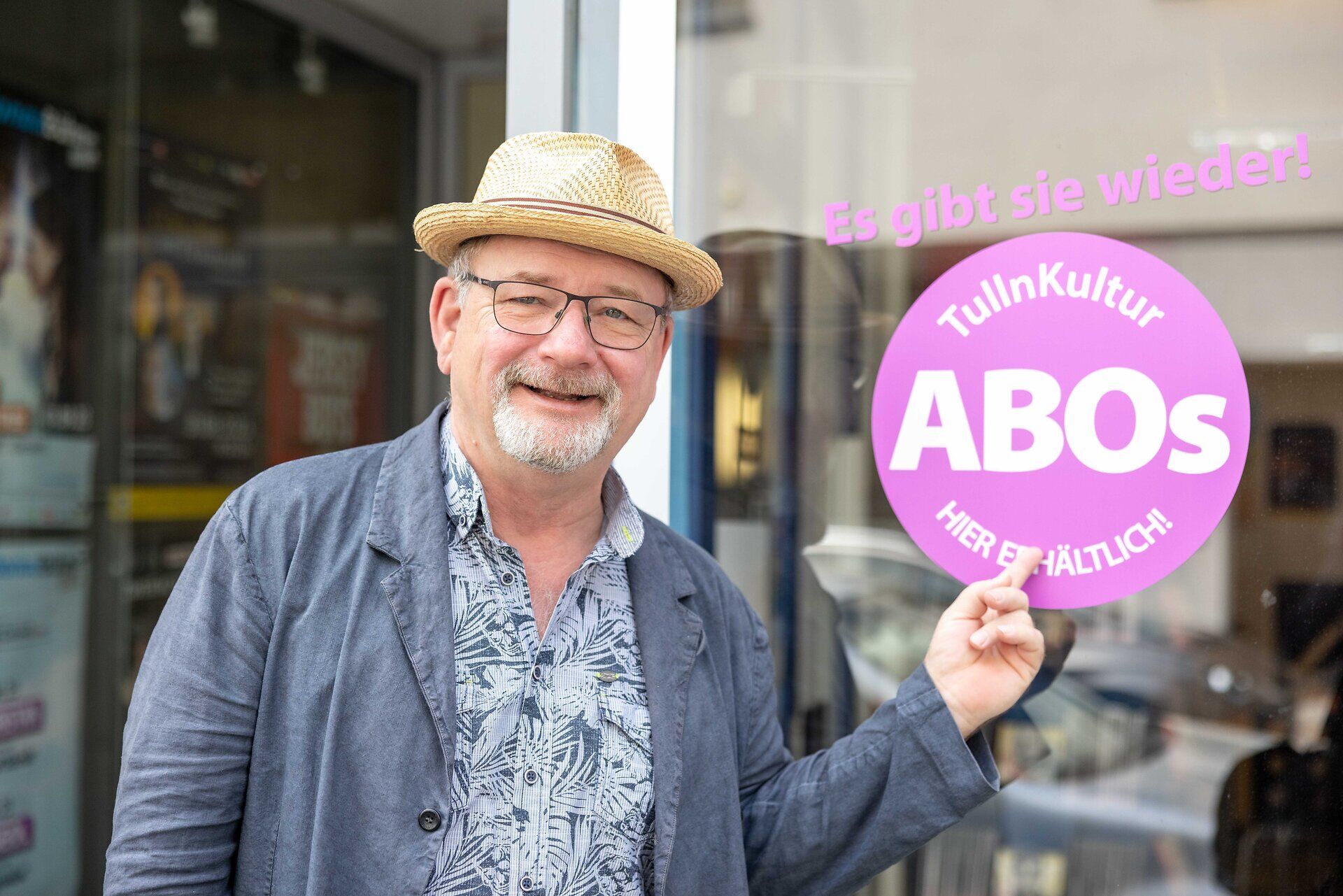 Mann steht vor einem Geschäft und zeigt auf einen Auflkleber "Tulln Kultur Abos"