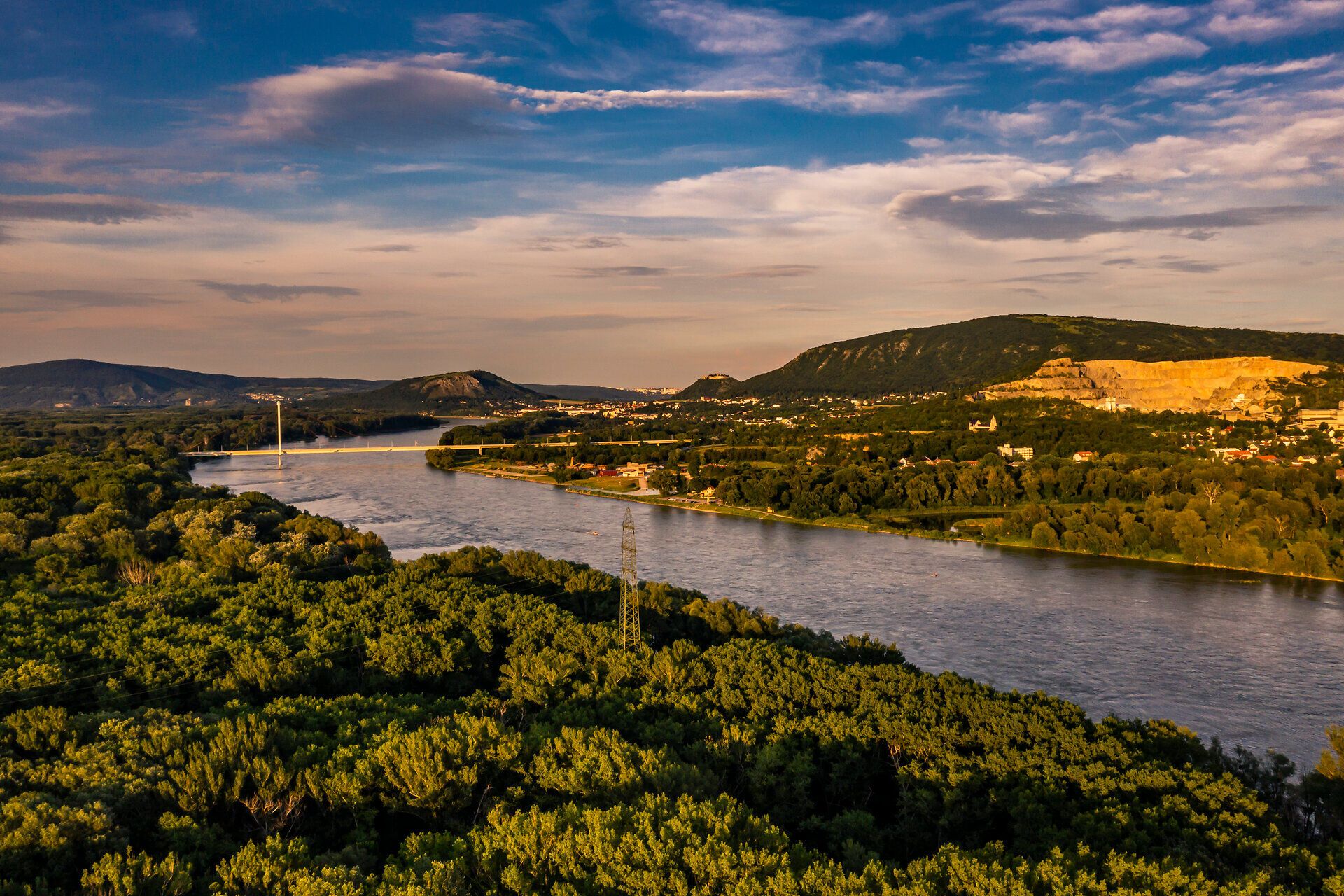 Die sanften Wellen der Donau schlängeln sich durch eine üppige, grüne Landschaft, die im warmen Licht des Sommers erstrahlt. Hoch oben erheben sich die sanften Hügel, während die Bäume im sanften Wind rauschen und eine friedliche Atmosphäre schaffen. Ein wahres Paradies für Naturliebhaber und Erholungssuchende.