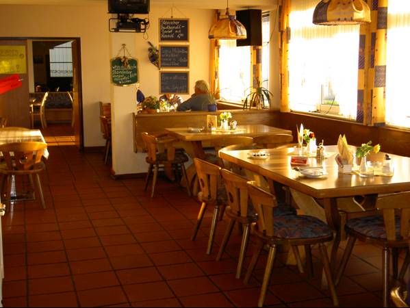 Gemütlicher Gastraum mit Holztischen und Stühlen, dekoriert mit Blumen und Servietten.