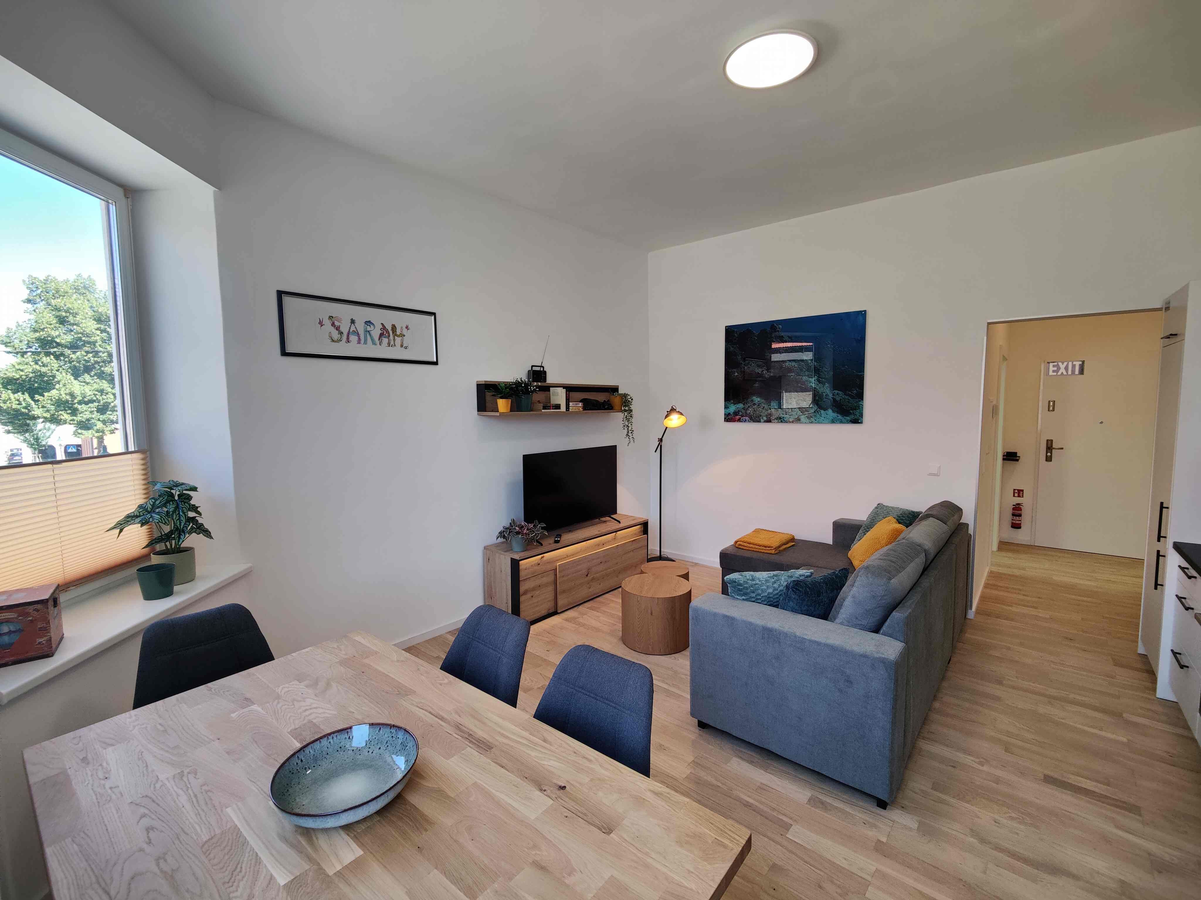 Wohnzimmer mit Couch und TV sowie Esstisch 