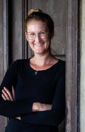 Die Winzerin Michaela Riedmüller lehnt an einer Wand.