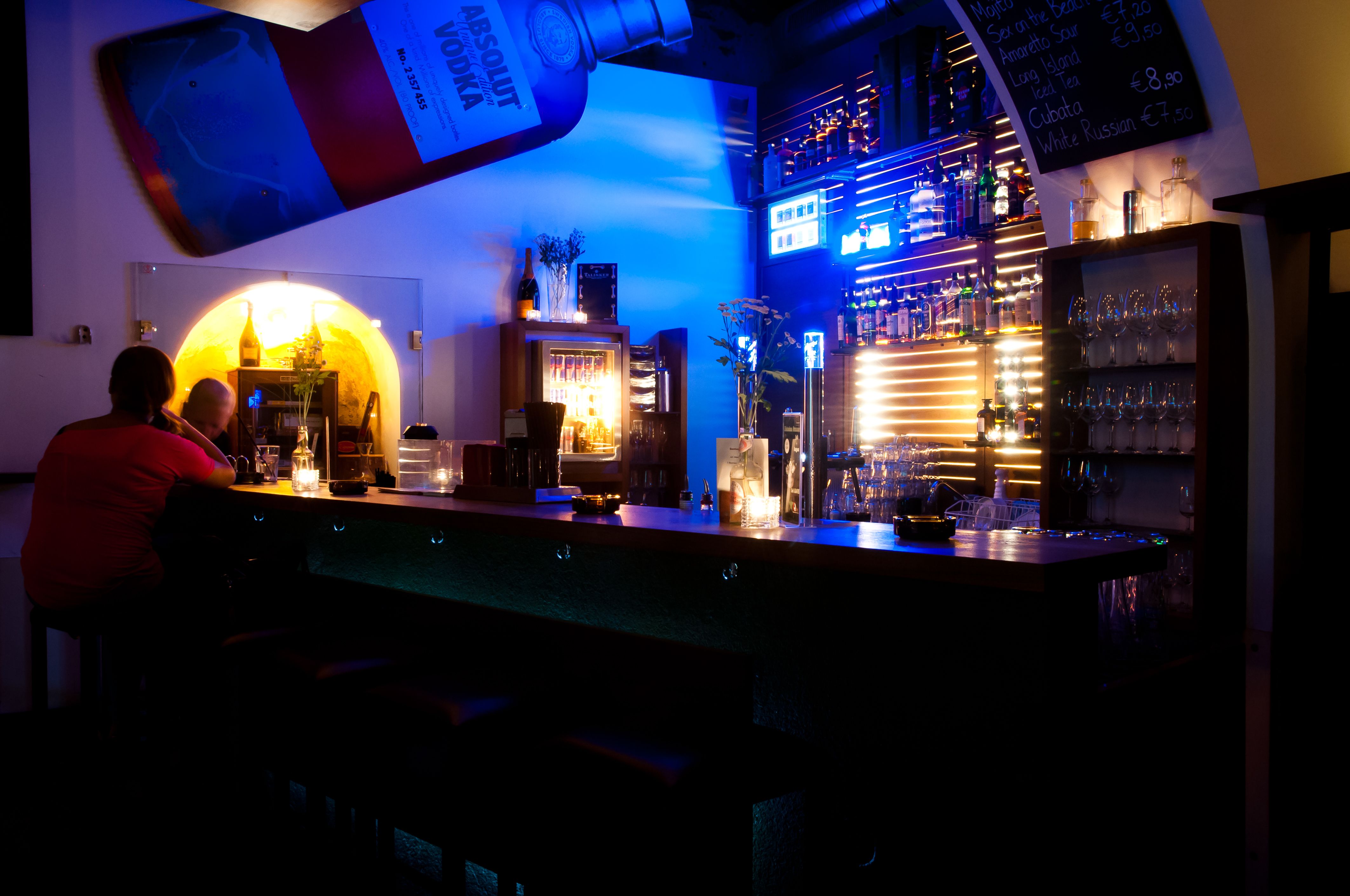 Innenansicht einer Bar mit blauer Beleuchtung und Flaschenregalen.