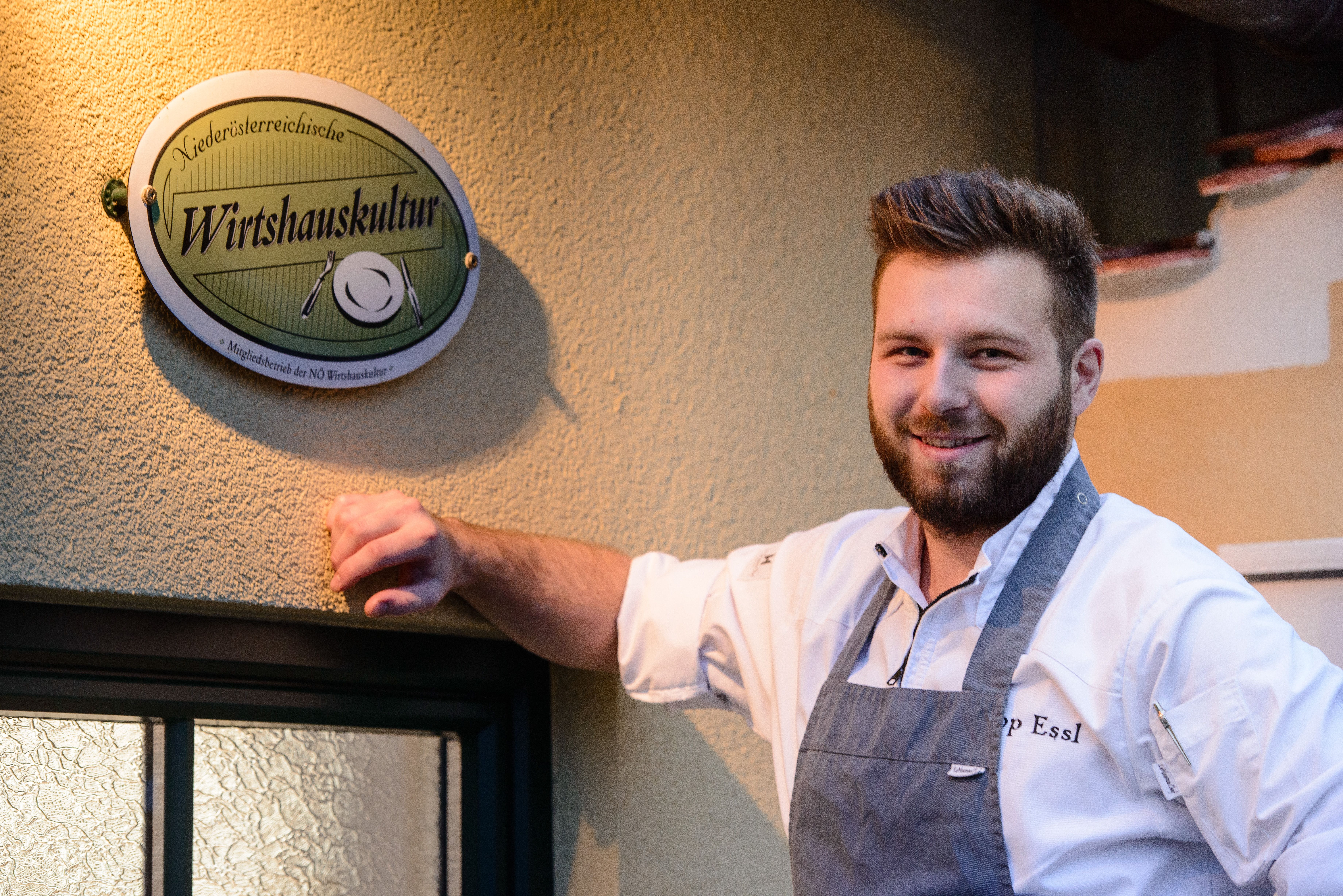 Philipp Essl in chef's clothes in front of a patterned wallpaper.