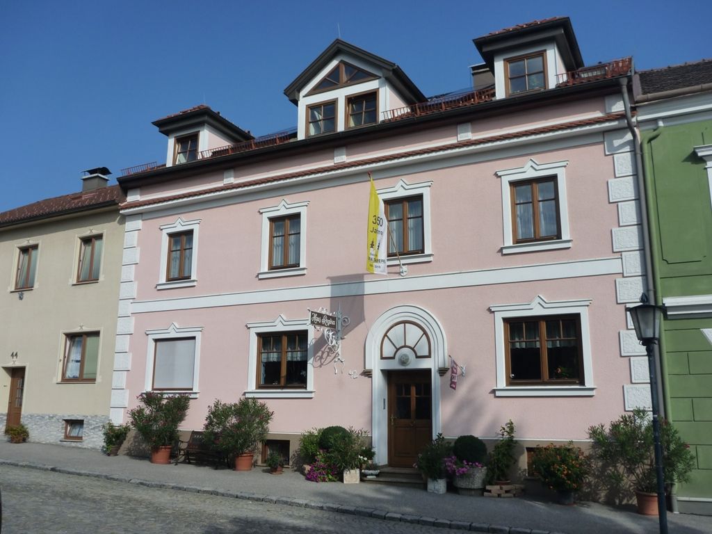 Außenansicht eines rosa Hauses mit weißen Fensterrahmen und einer gelben Fahne.