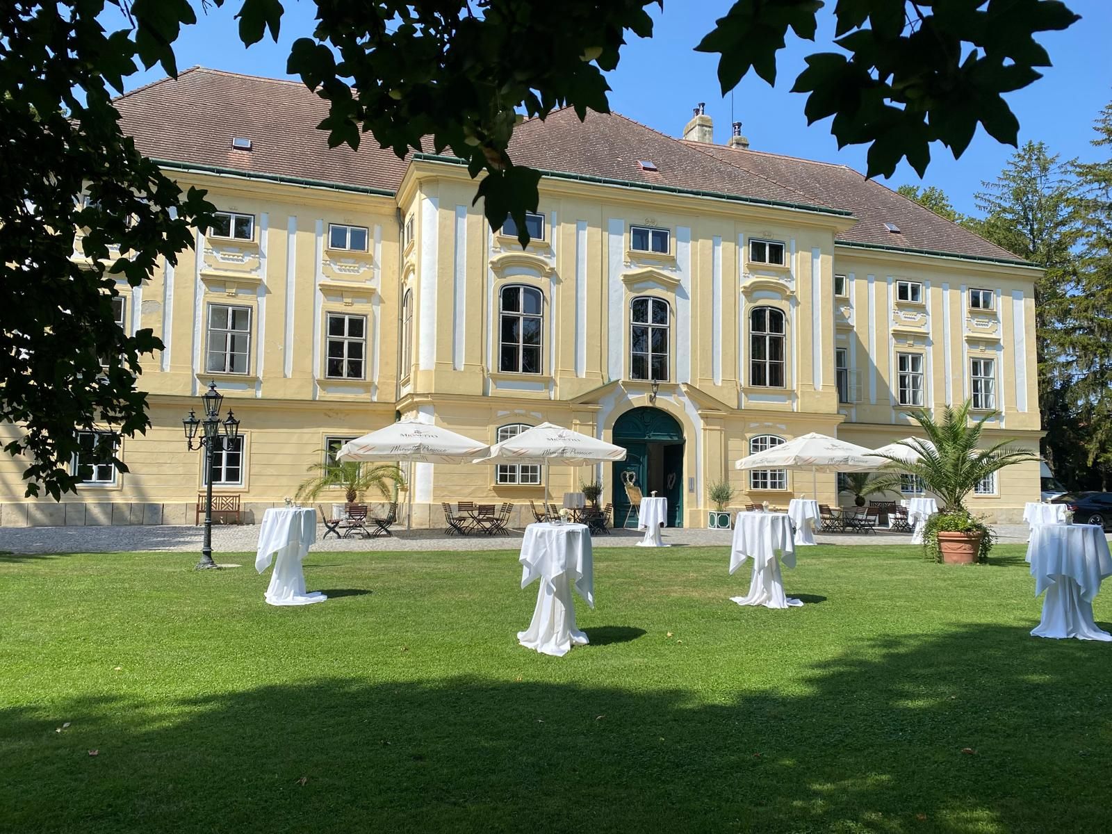 Außenansicht Schloss, im Vordergrund eine Wiese mit weißen Stehtischen und weißen Sonnenschirmen