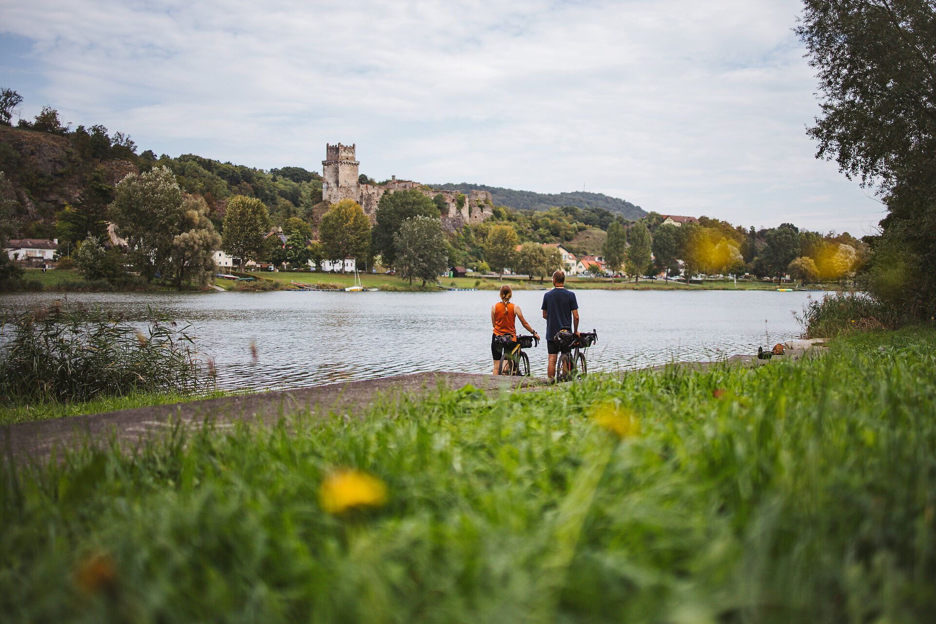Am Ufer der Donau genießen Radfahrer die friedliche Atmosphäre und die malerische Landschaft. Die sanften Hügel und das glitzernde Wasser laden zu einer entspannten Auszeit ein, während die Natur in voller Blüte steht.