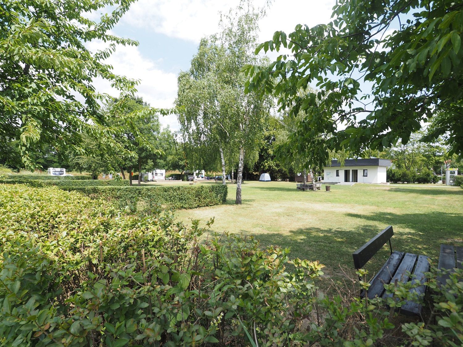 Stellplatz auf einer frisch gemähten Wiese. Om Hintergrund ein Häuschen für Sanitäranlage.