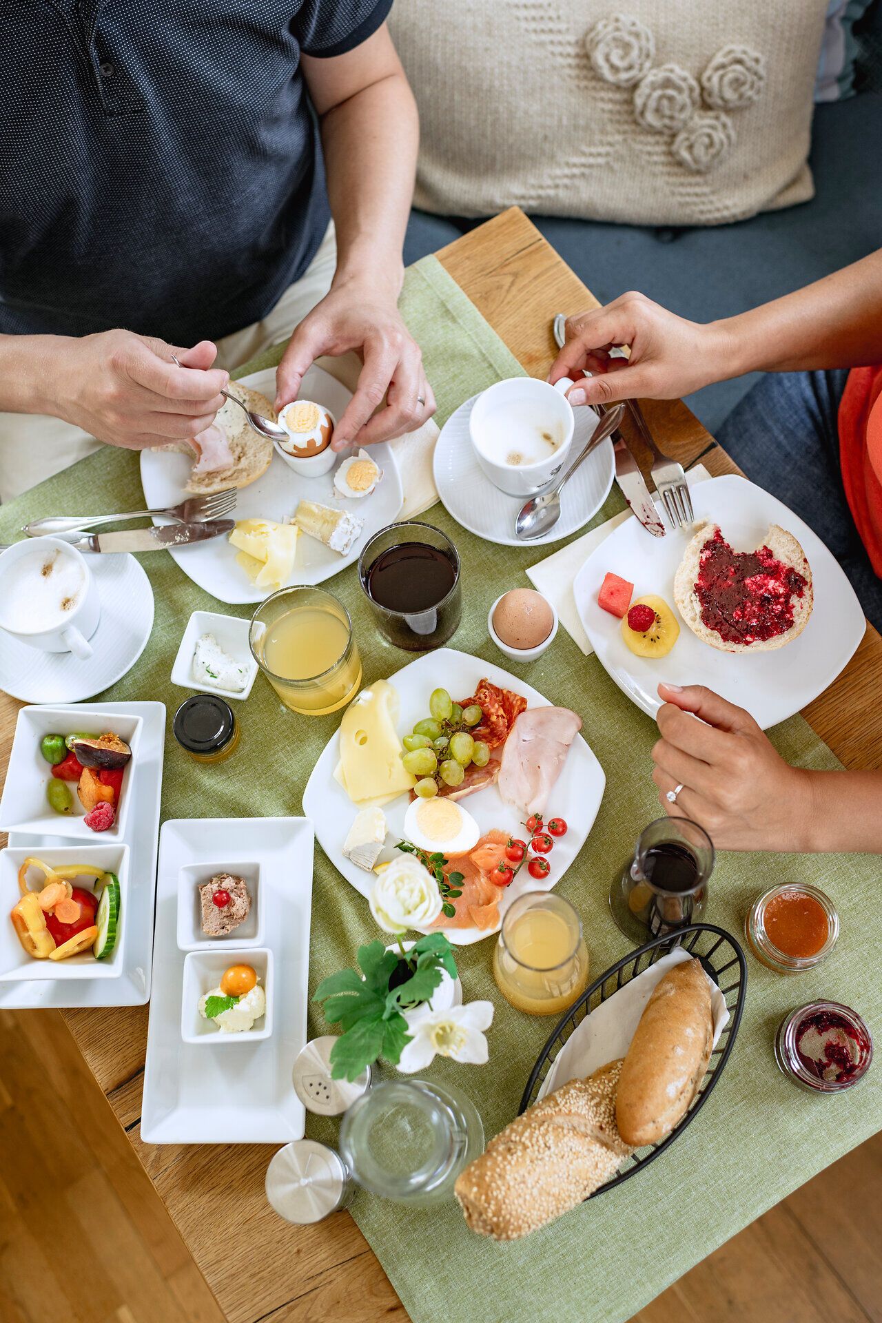 Gedeckter Frühstückstisch, Hände öffnen ein Frühstücksei und greifen zur Kaffeetasse.