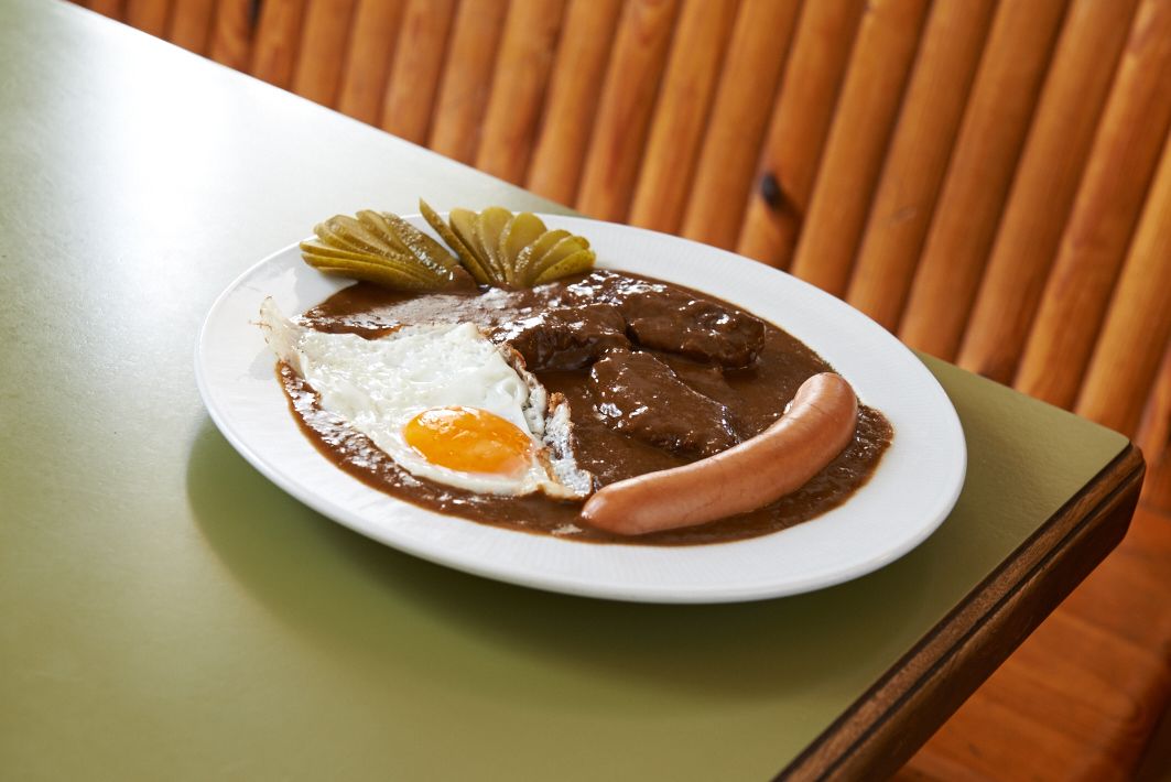 Ein Teller mit Bratensauce, Spiegelei, Wurst und Gurkenscheiben.