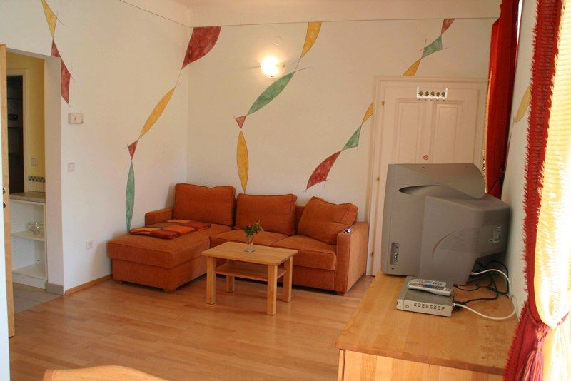 Wohnzimmer mit oranger Couch, Holztisch, Fernseher und bunter Wanddekoration.