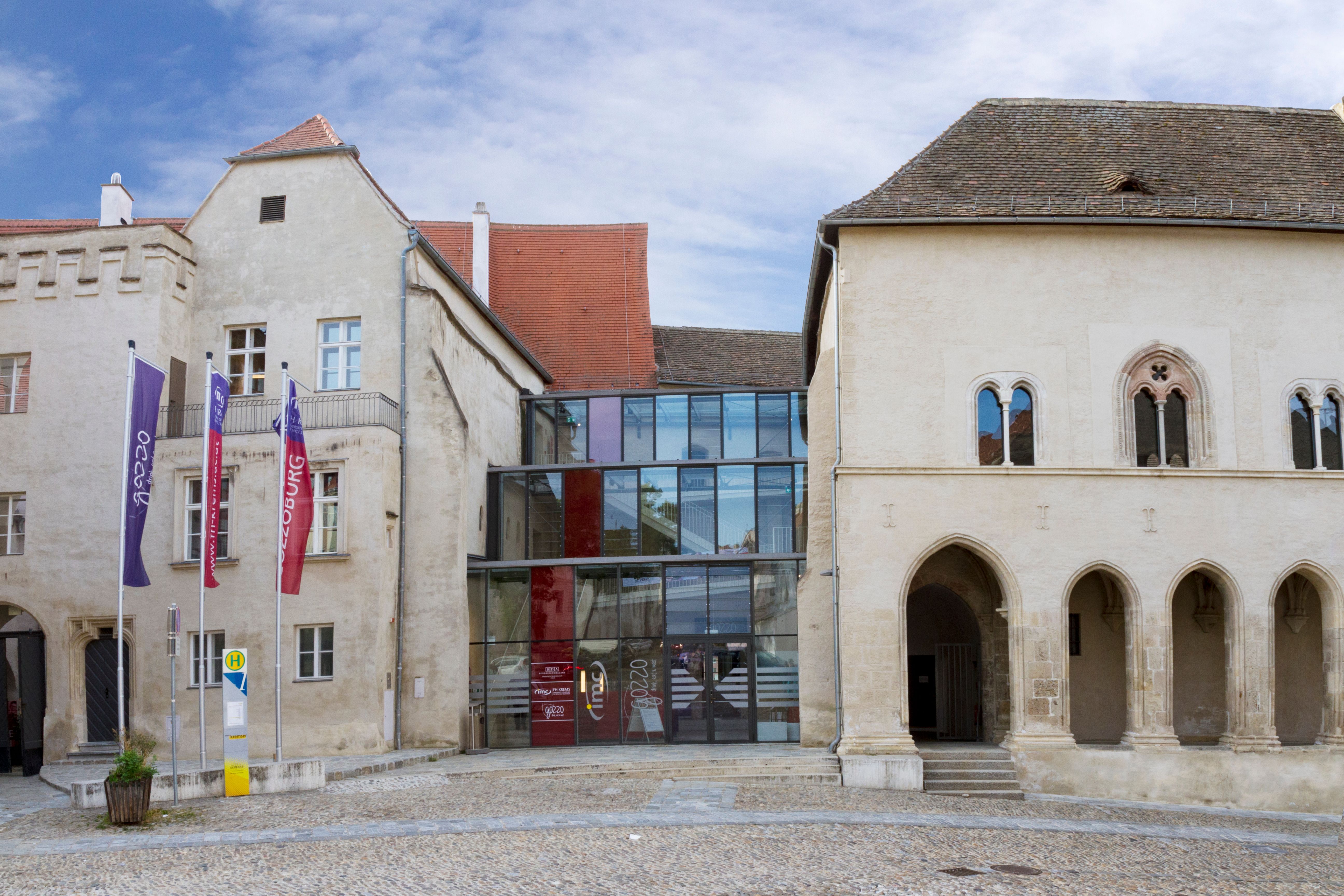 Historisches Gebäude mit modernem Glaszwischenbau, Kopfsteinpflaster im Vordergrund.