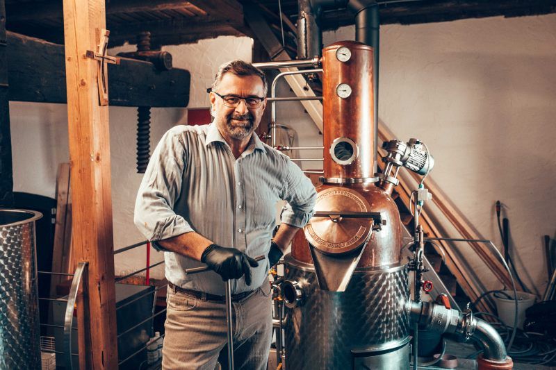 A man stands next to a copper still in a distillery.