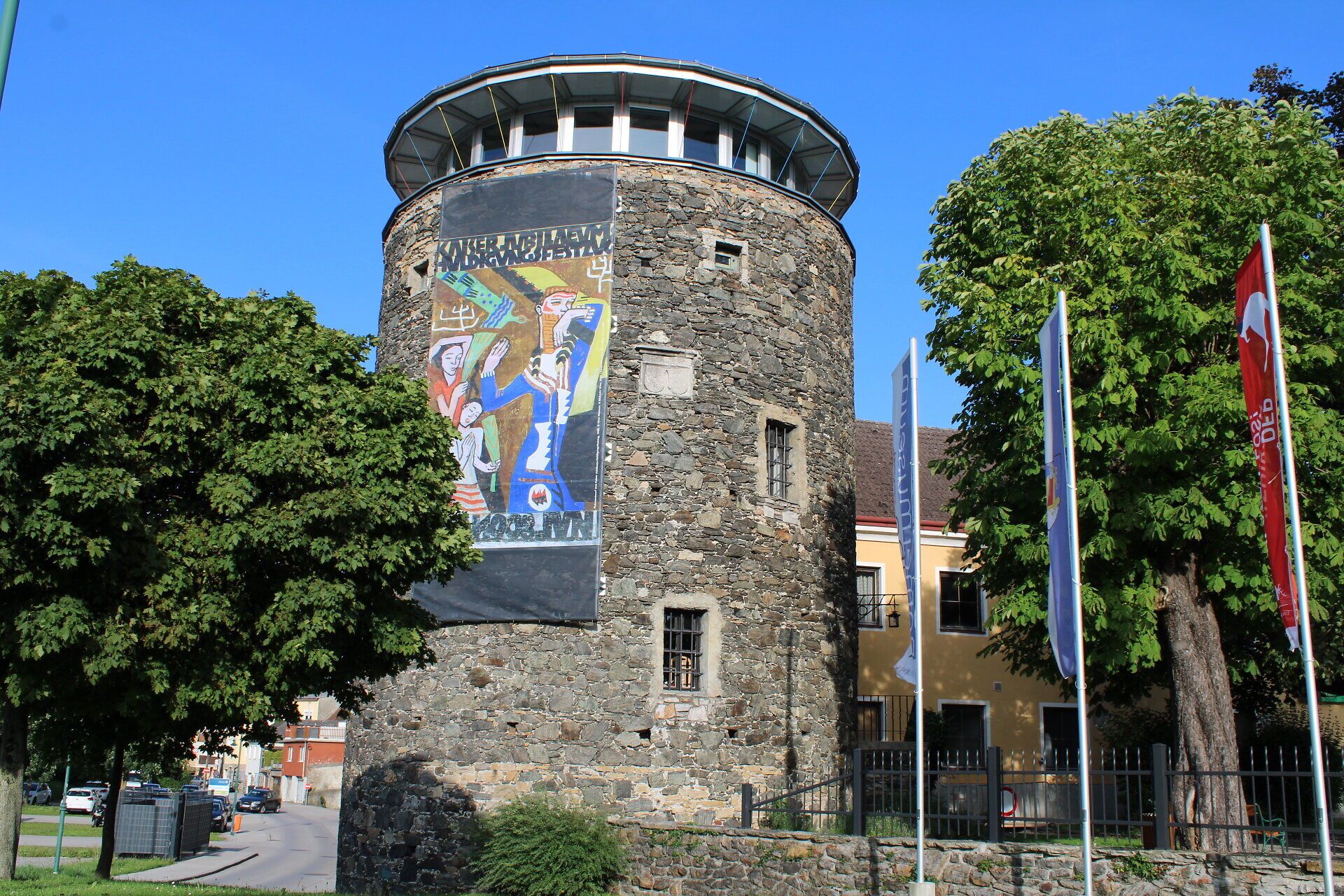Der majestätische Welserturm erhebt sich stolz über die sanften Hügel und die glitzernde Donau. Umgeben von üppigem Grün und bunten Fahnen, lädt dieser historische Ort dazu ein, die atemberaubende Aussicht zu genießen und die Seele baumeln zu lassen.