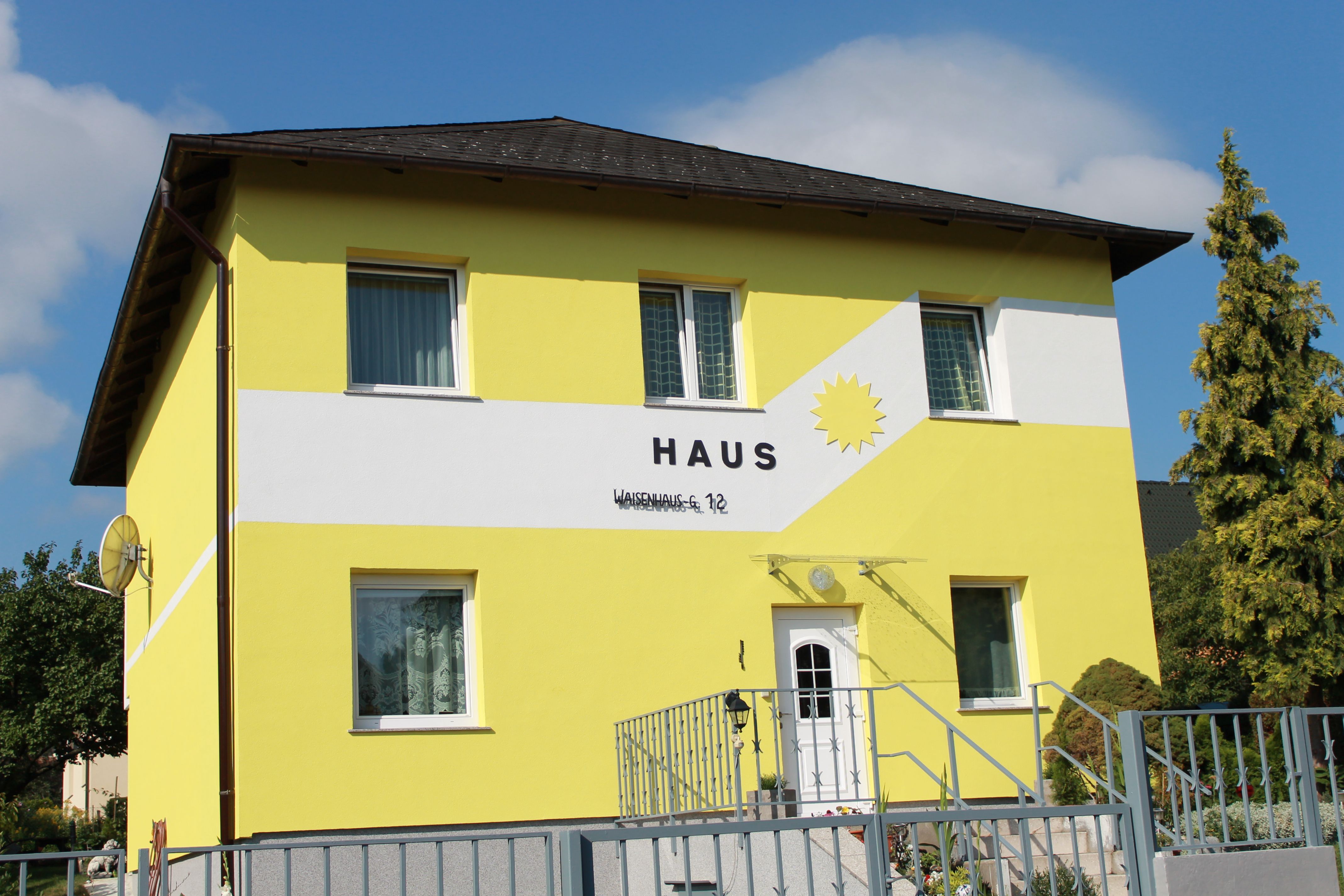 Yellow house with the inscription 'Haus' and a sun on the façade.