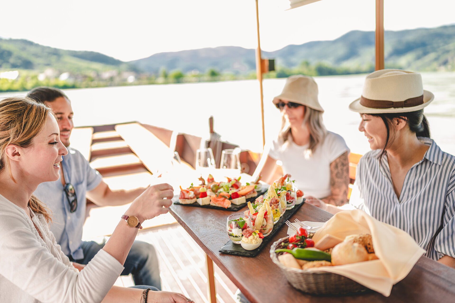 Vier Personen sitzen auf einer Zille und auf dem Holztisch stehen bunte Häppchen.
