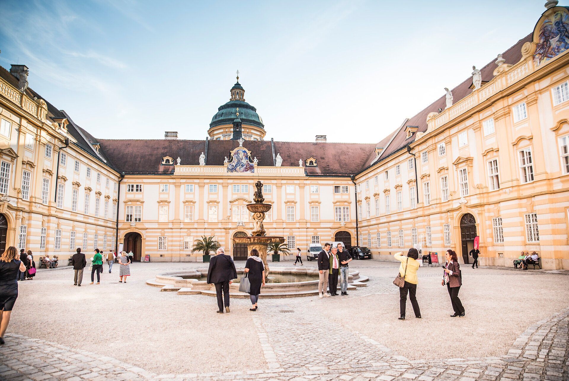 Die barocke Pracht des Stifts Melk entfaltet sich in voller Schönheit, während Besucher durch den malerischen Innenhof schlendern. Die harmonische Verbindung von Architektur und Natur schafft eine einladende Atmosphäre, die zum Verweilen einlädt.