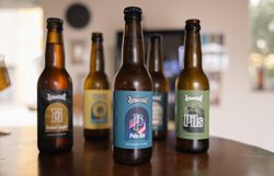 Mehrere Braustall-Bierflaschen verschiedener Sorten auf einem Holztisch, im Vordergrund eine Flasche Pale Ale.