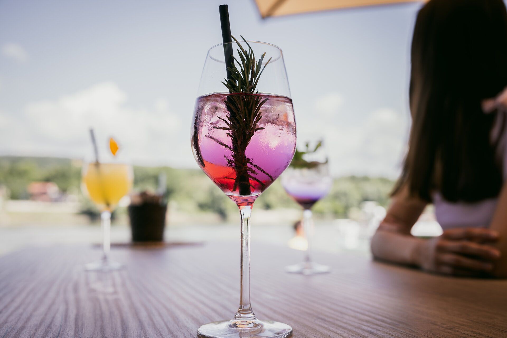 Ein Cocktailglas mit lila Flüssigkeit und Zweig mit Strohhalm steht auf einem Tisch