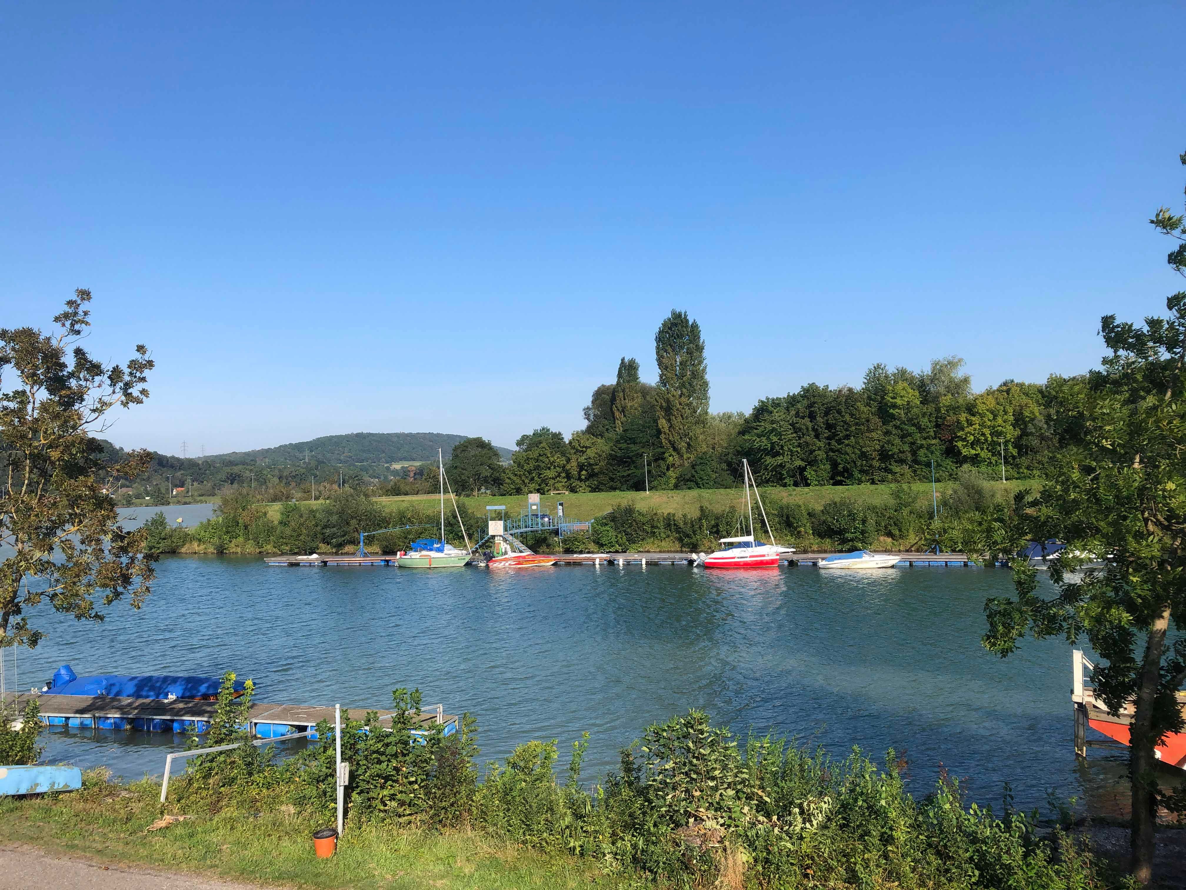 Boote an einer Anlegestelle am Fluss mit Bäumen im Hintergrund.