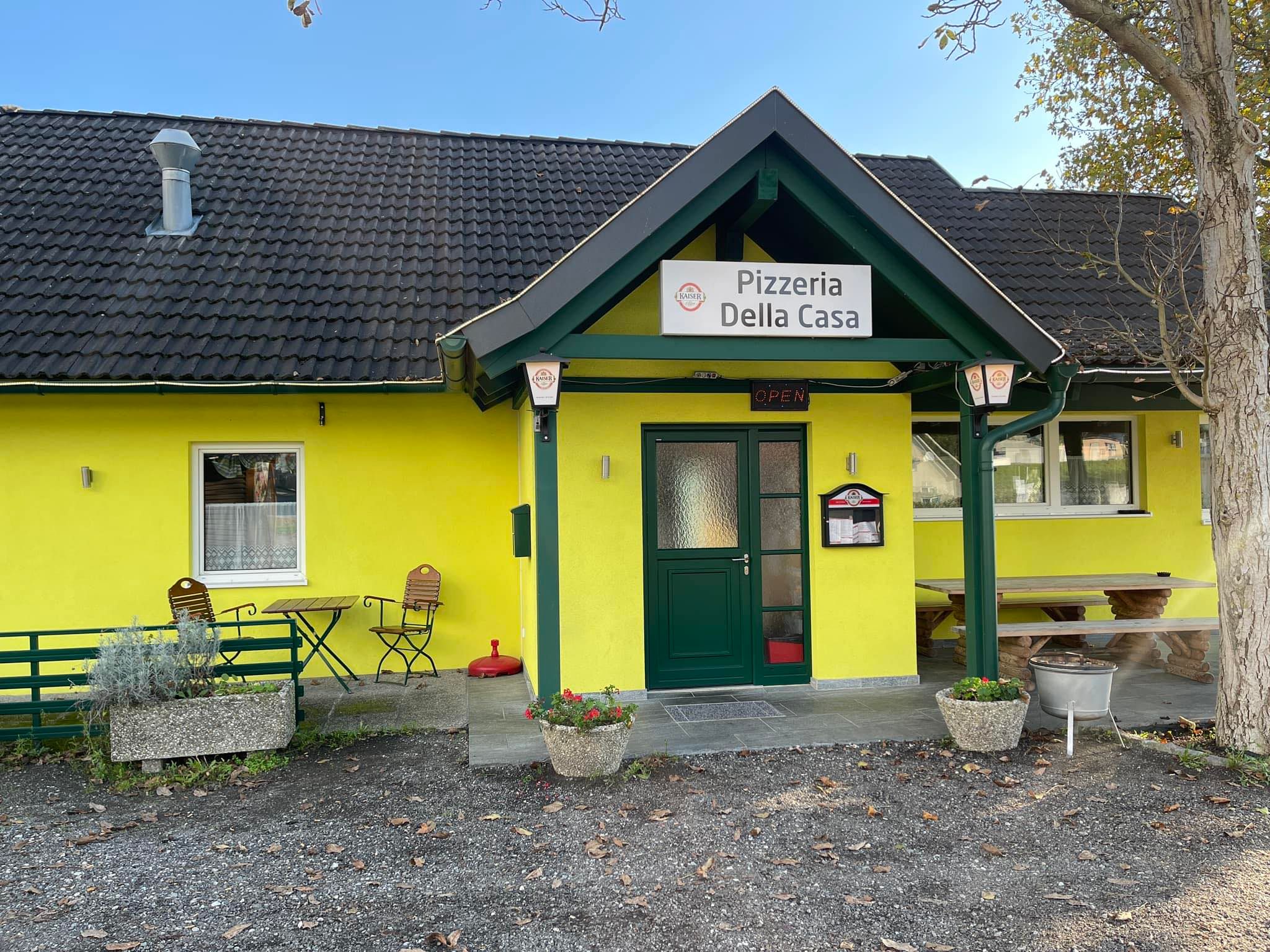 Außenansicht einer gelben Pizzeria mit dem Namen 'Pizzeria Della Casa'.