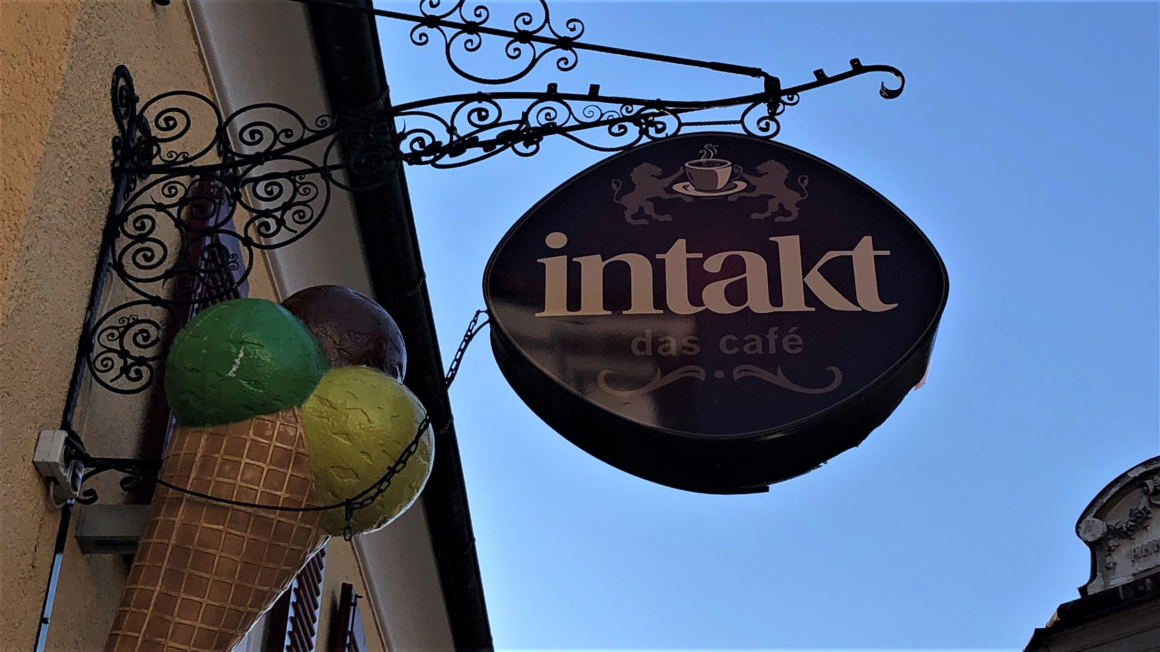 Schild des Cafés Intakt mit Eiswaffel-Dekoration an einer Hauswand.